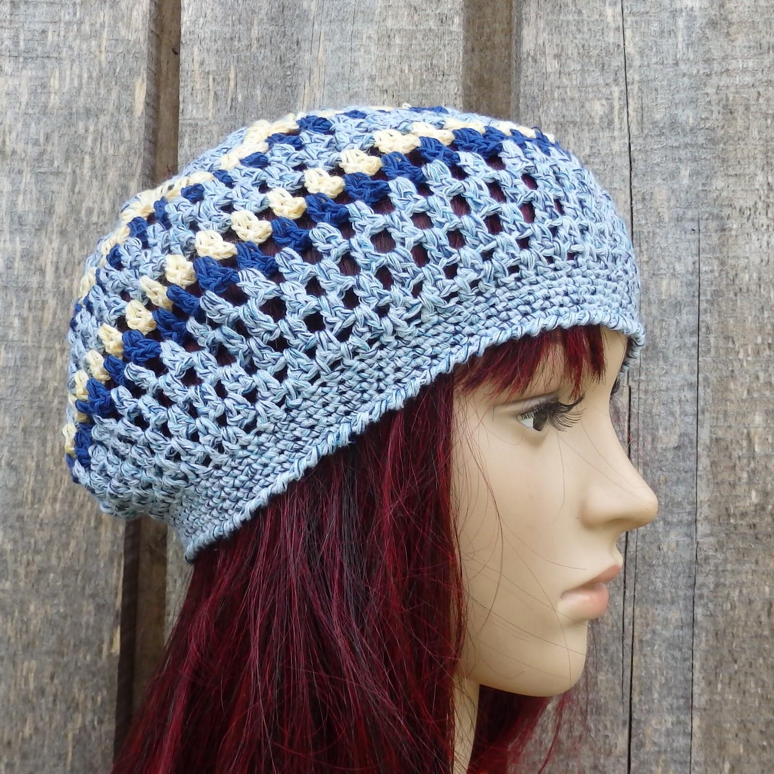 Blue and beige crocheted hat worn by a mannequin against a wooden background