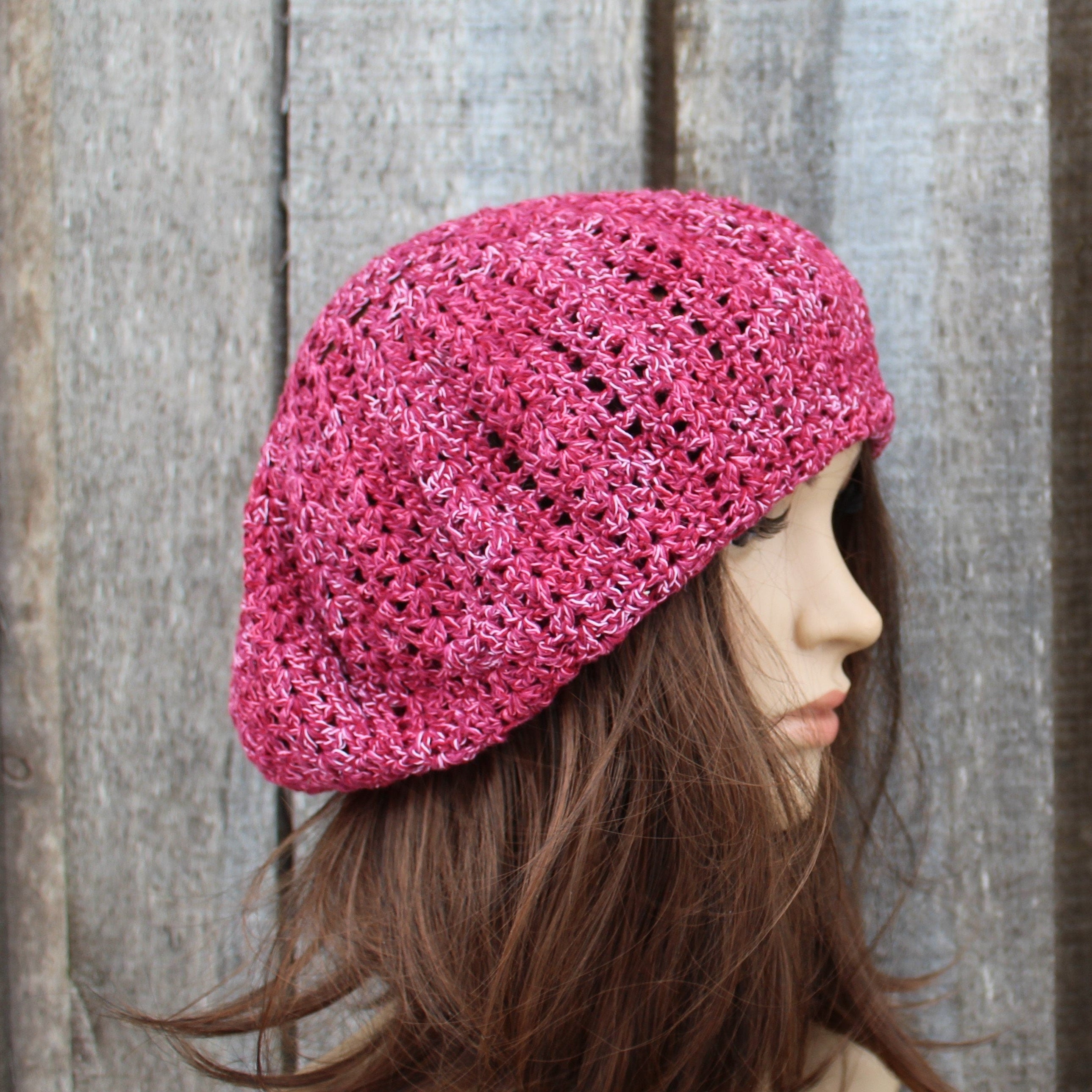 Pink knitted beret worn by a mannequin against a wooden background