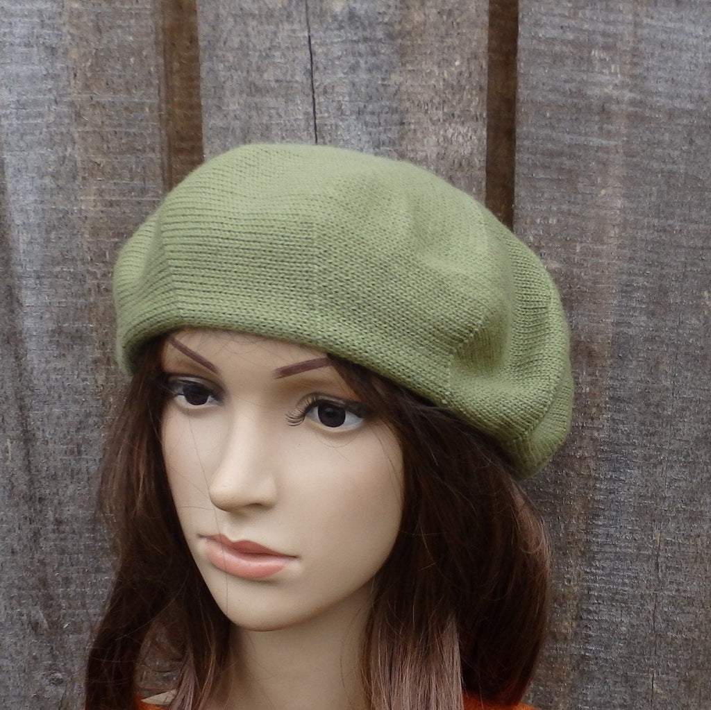 Green knitted beret on a mannequin head against a wooden background
