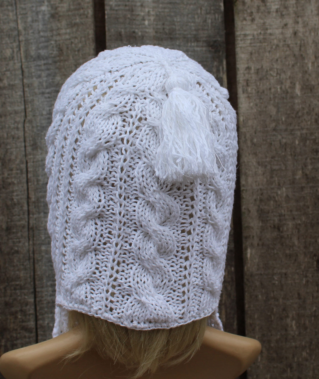 White knitted bonnet on a mannequin head against a wooden background
