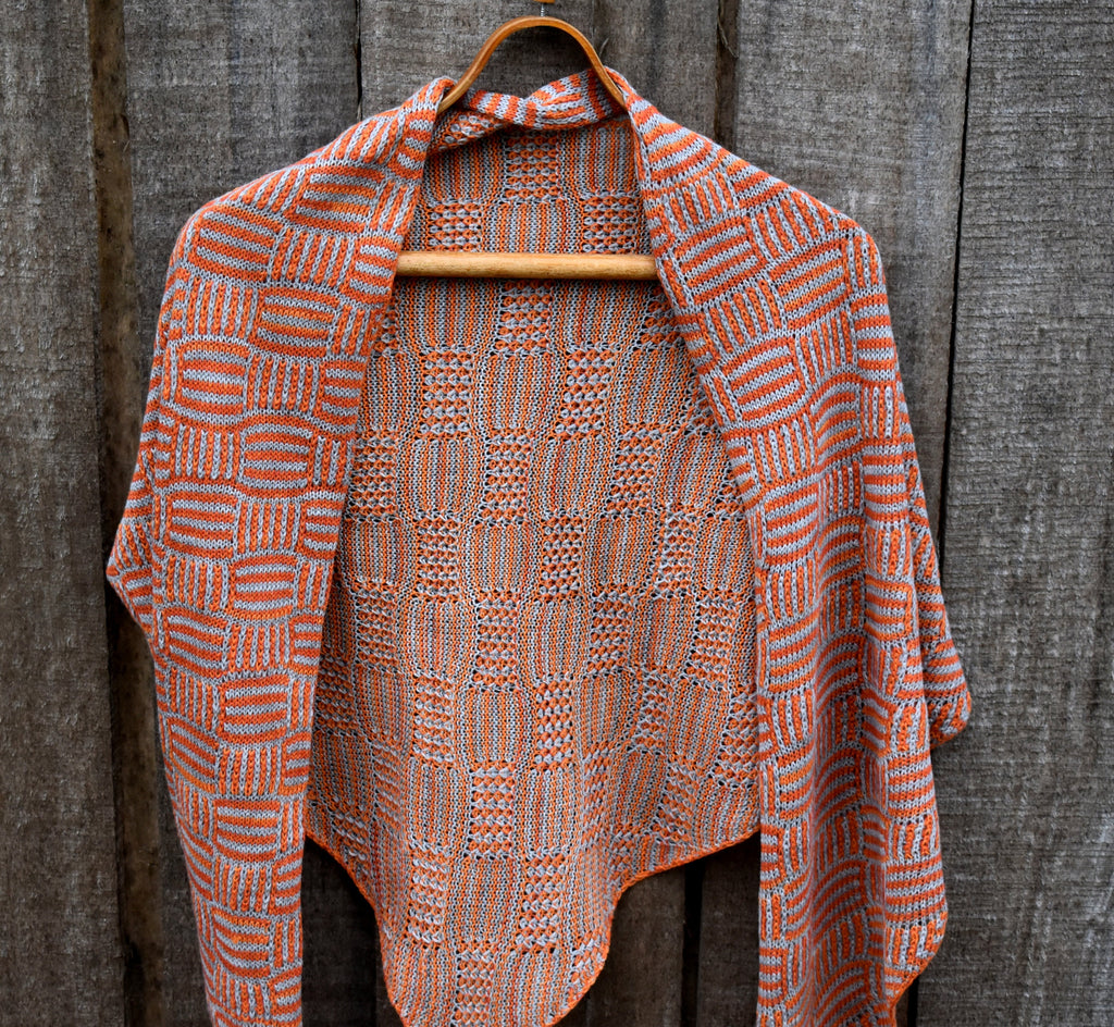 Knitted shawl with geometric pattern on a wooden hanger against a wooden background