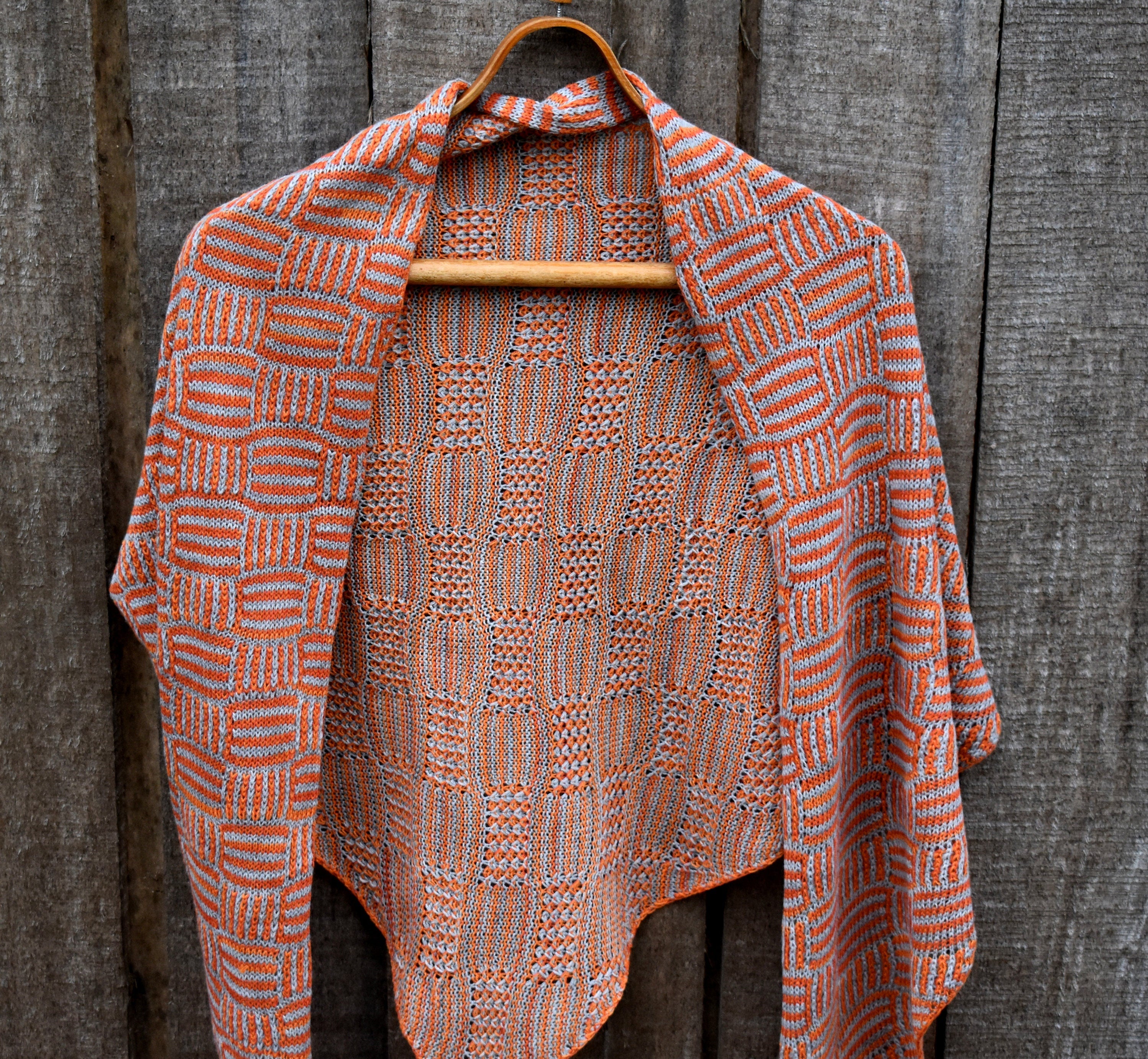 Knitted shawl with geometric pattern on a wooden hanger against a wooden background