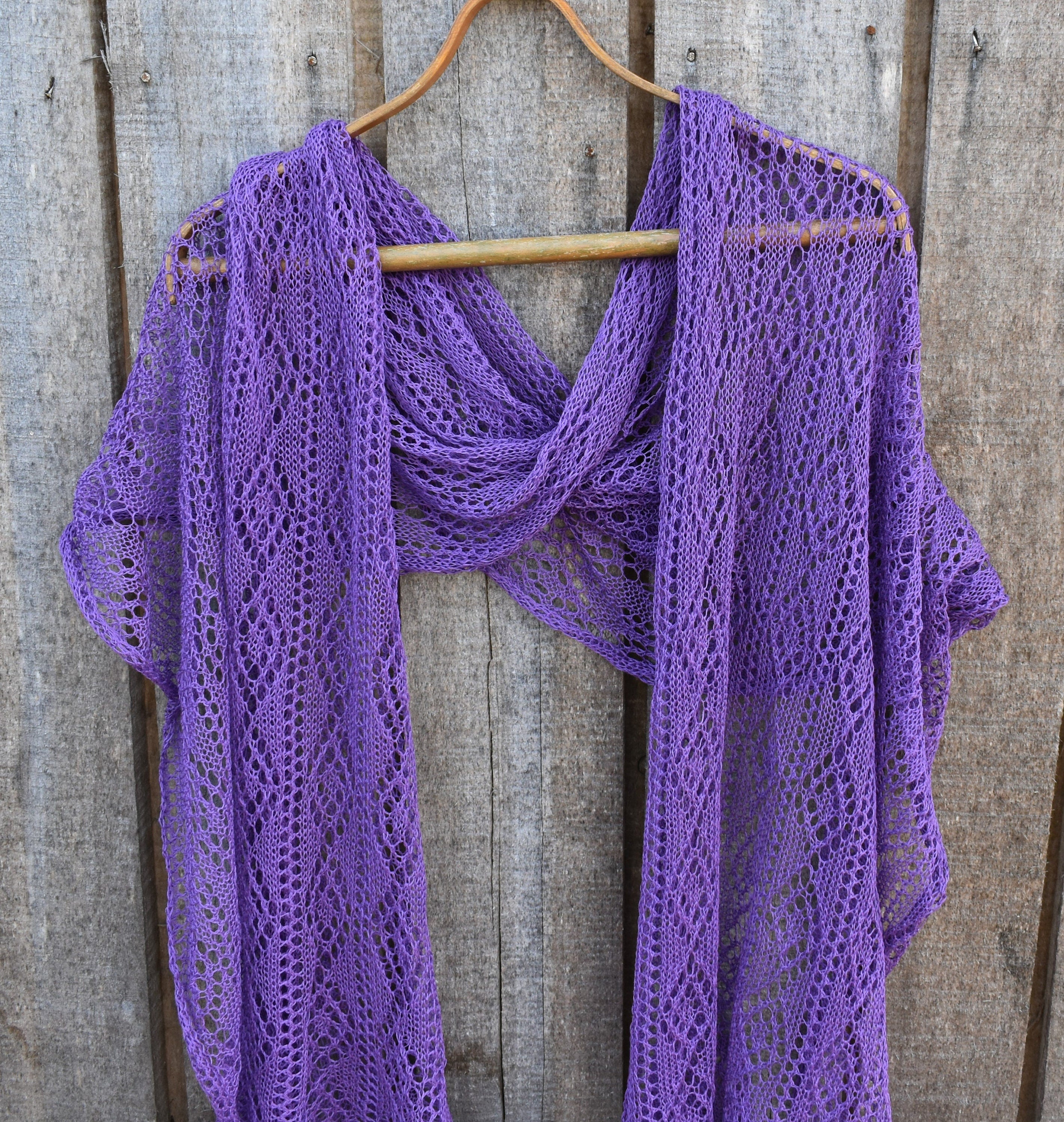 Purple knitted shawl on a wooden hanger against a wooden background