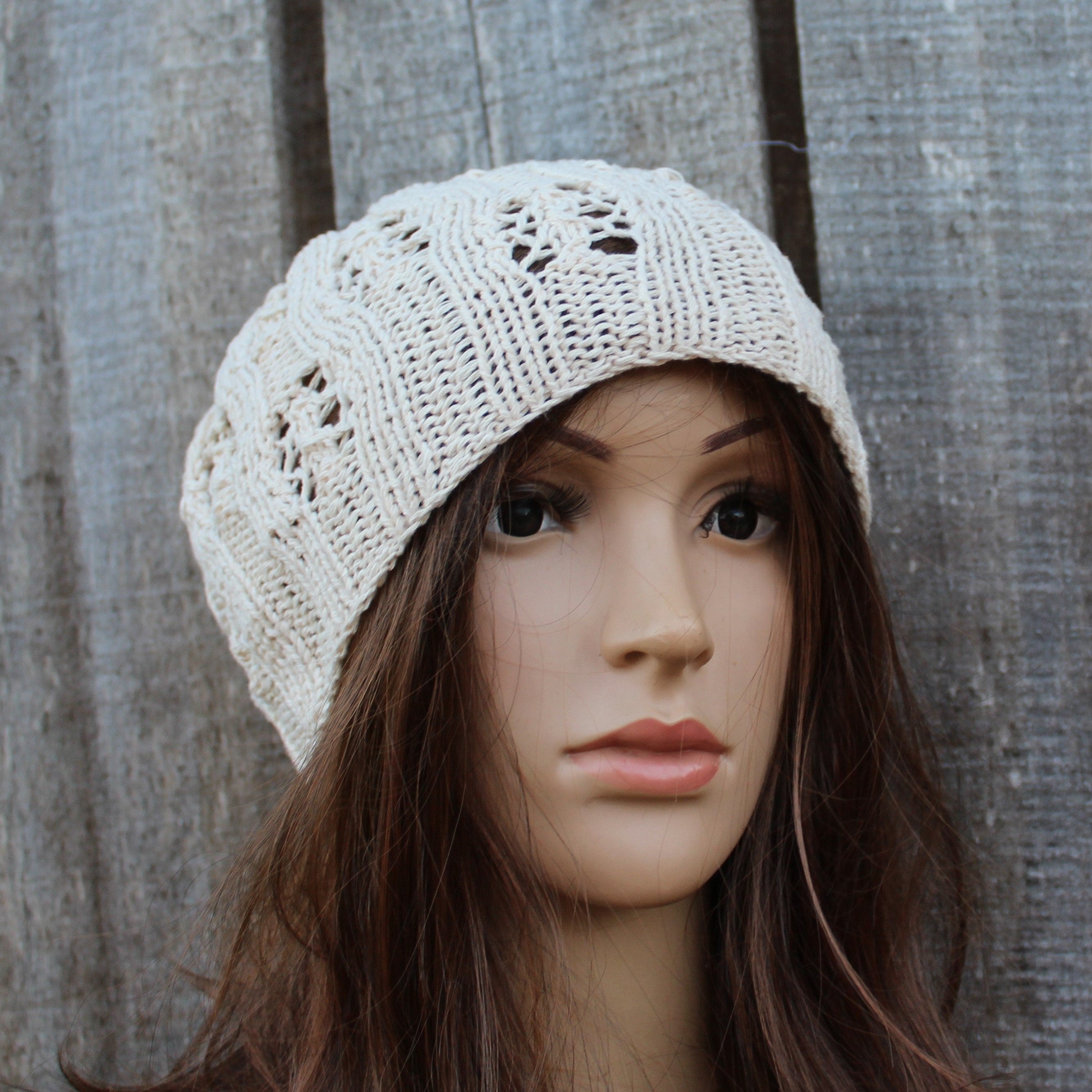 Mannequin head wearing a cream knitted hat against a wooden background