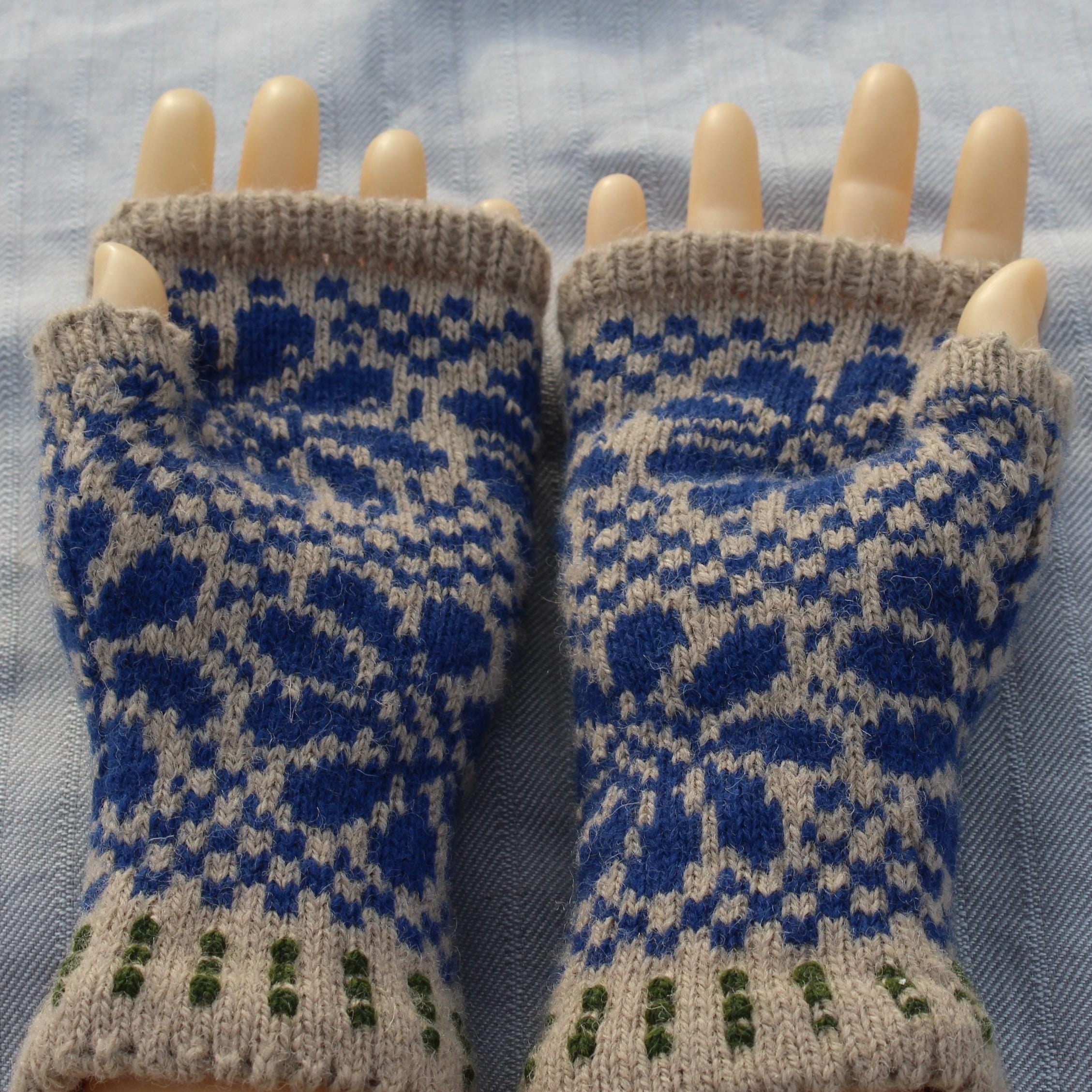 Pair of blue and beige patterned fingerless gloves on a light blue fabric background