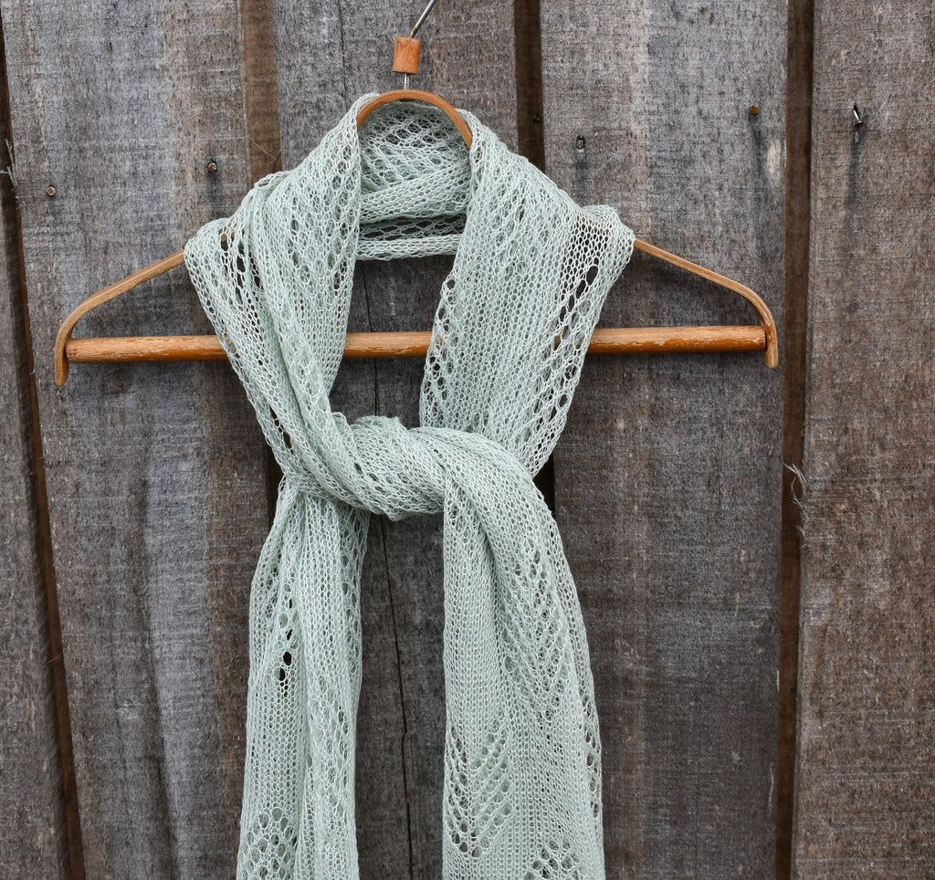 Light green knitted scarf on a wooden hanger against a wooden background