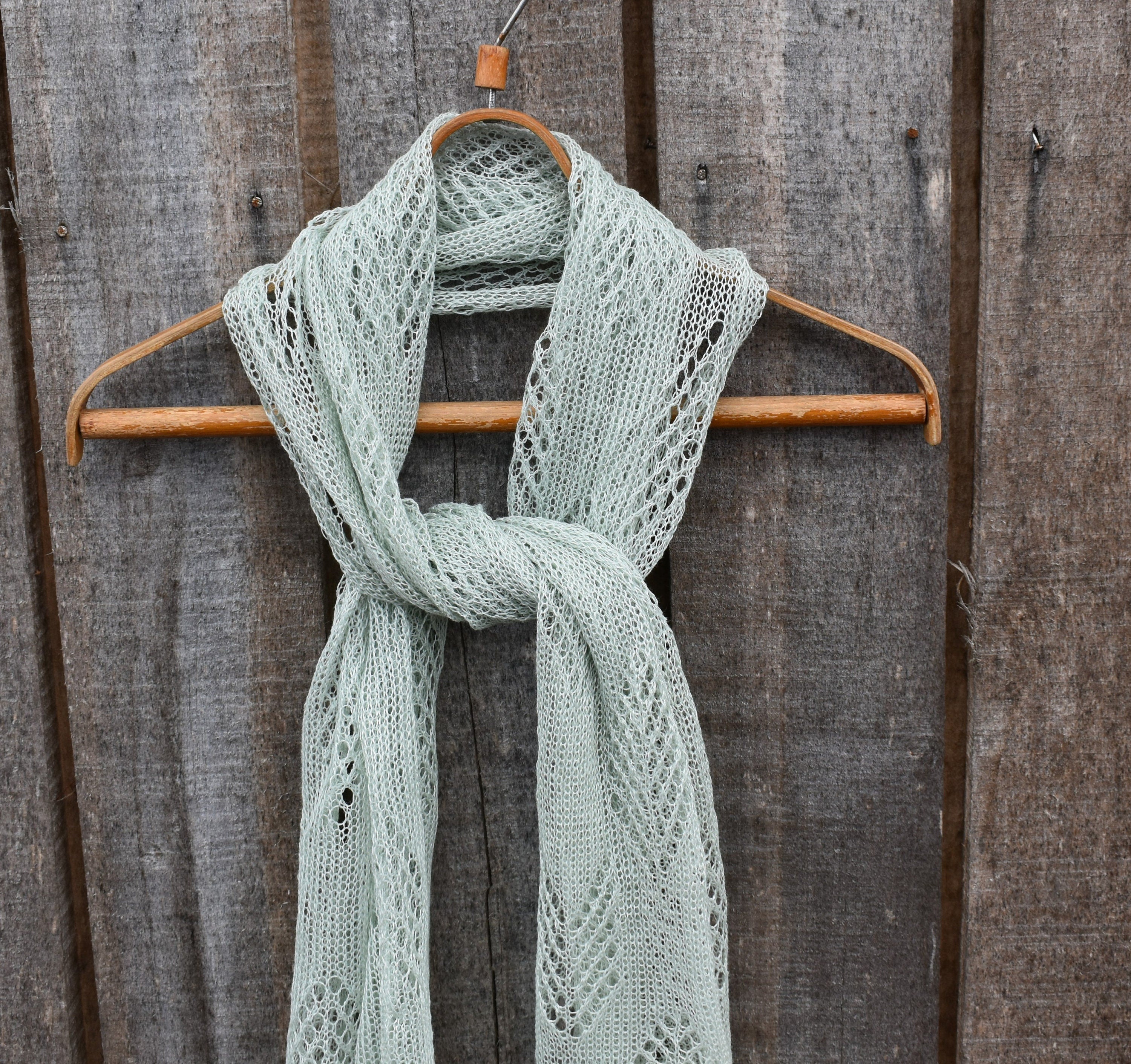 Light green knitted scarf on a wooden hanger against a wooden background