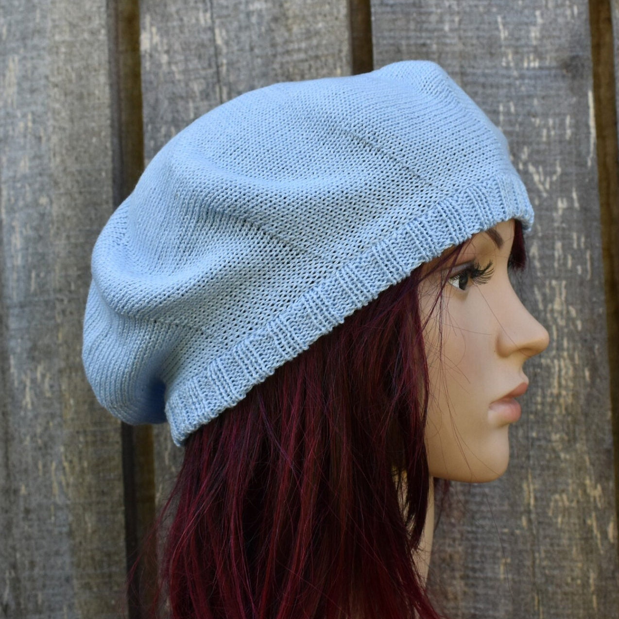 Light blue knitted beret on a mannequin head against a wooden background