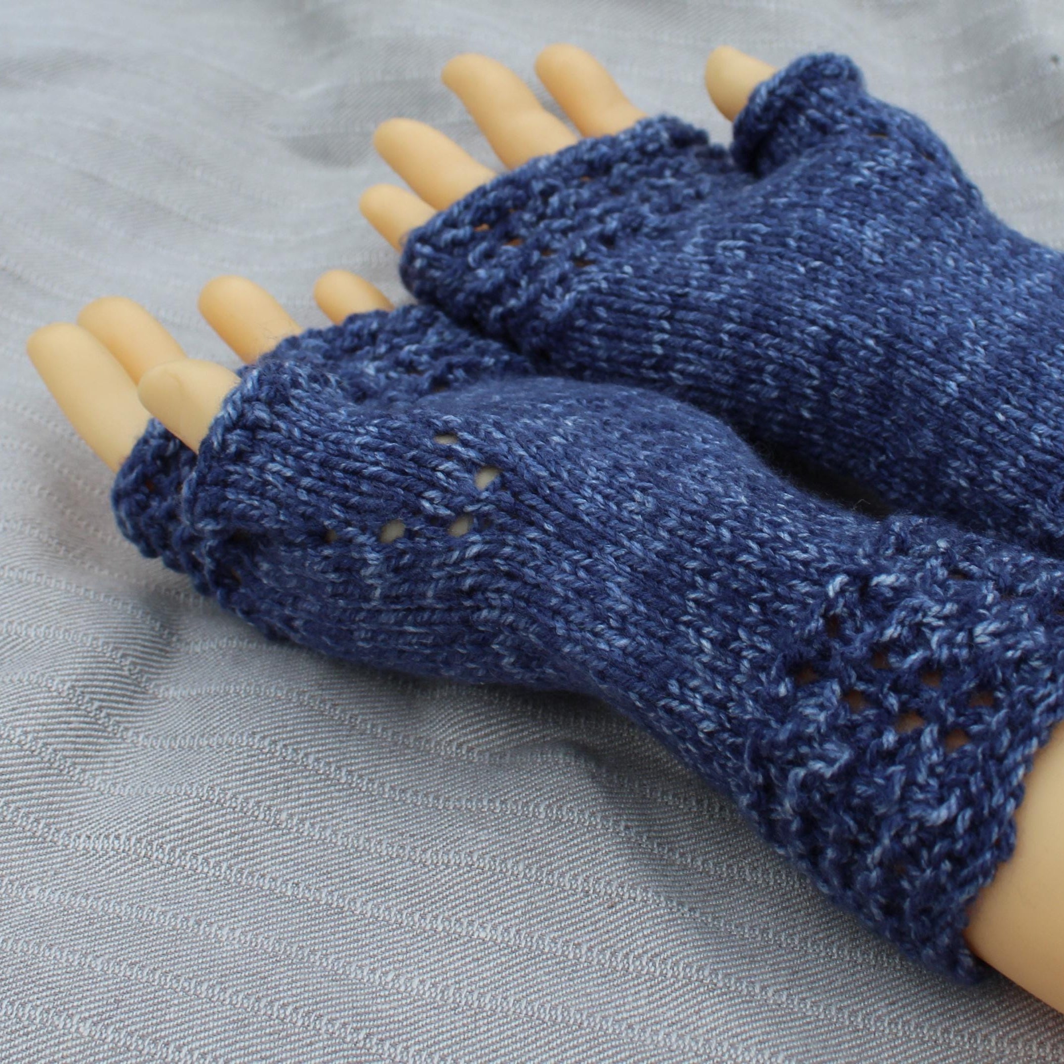 Blue knitted fingerless gloves on a mannequin hand against a gray background