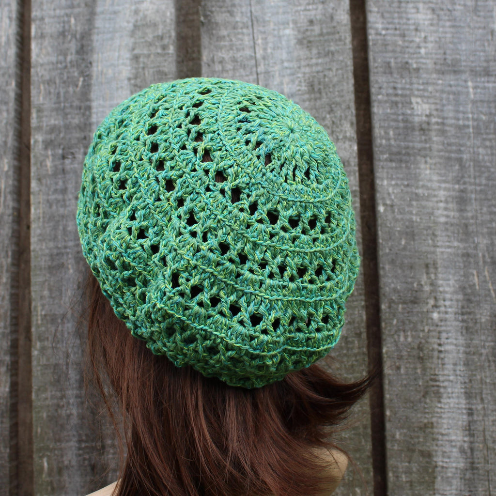 Green knitted beanie worn by a person against a wooden background