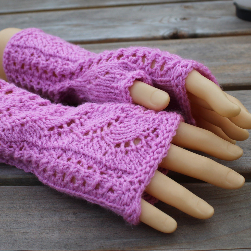 Pink knitted fingerless gloves on a mannequin hand against a wooden background