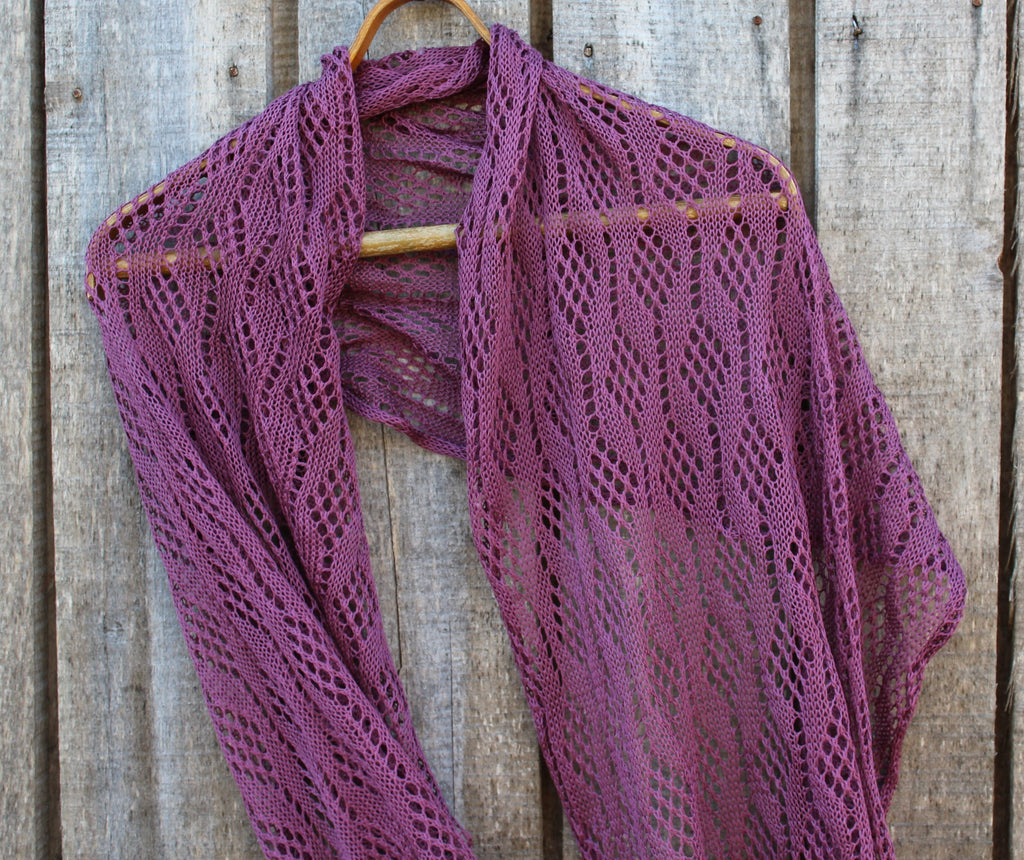 Purple knitted shawl on a wooden hanger against a wooden background