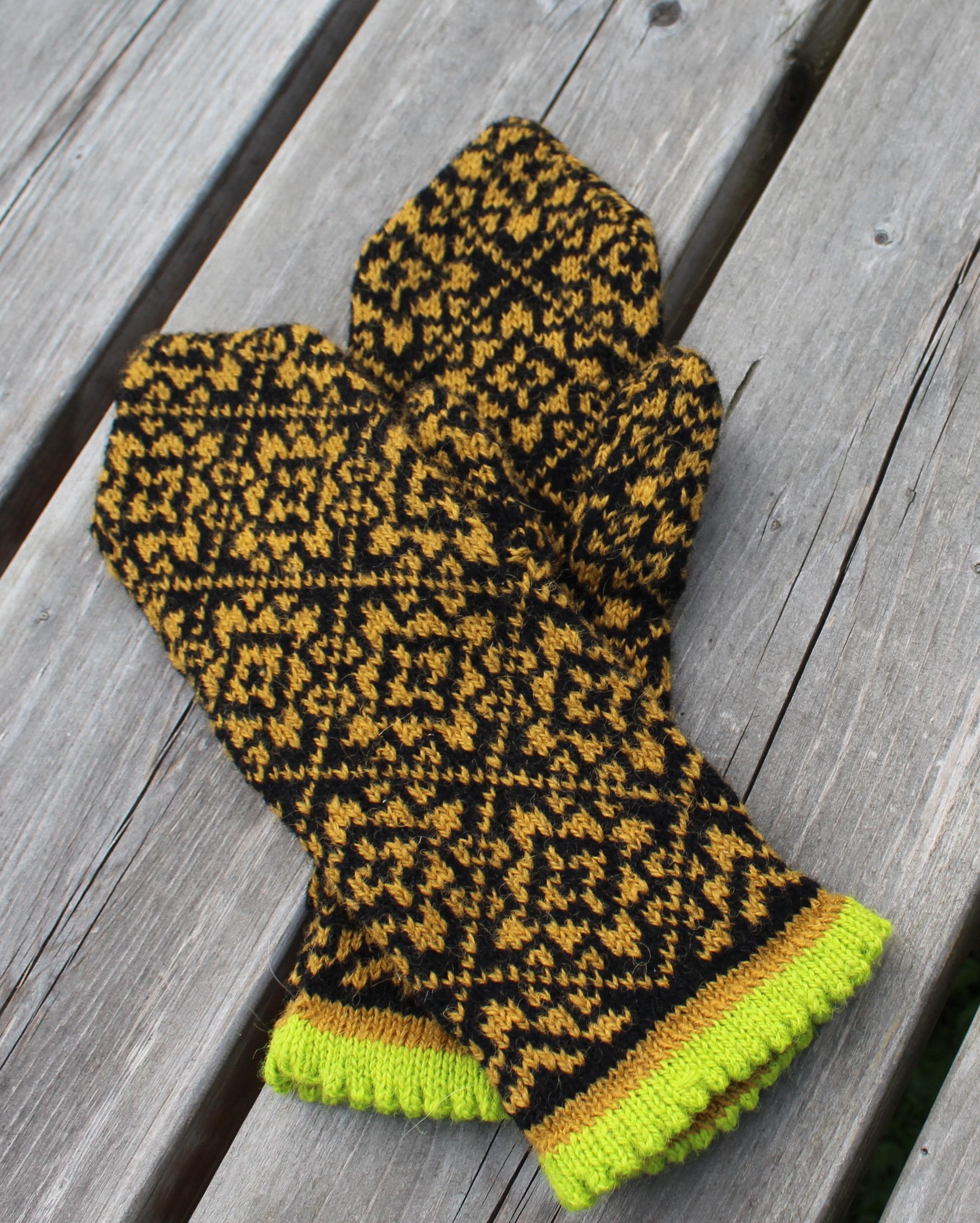 Knitted mitten with black and yellow pattern on a wooden surface