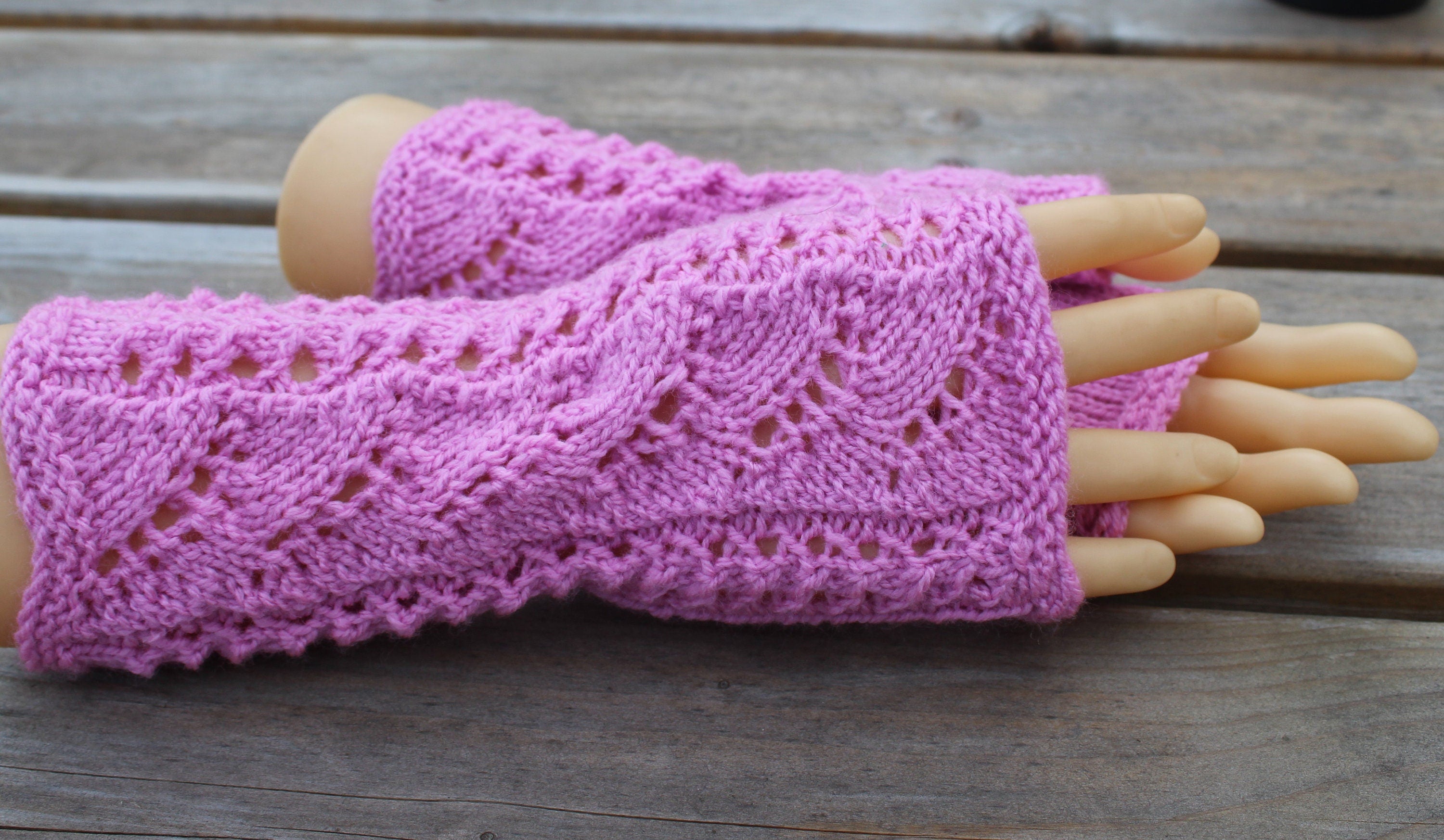 Pink knitted fingerless gloves on a wooden surface