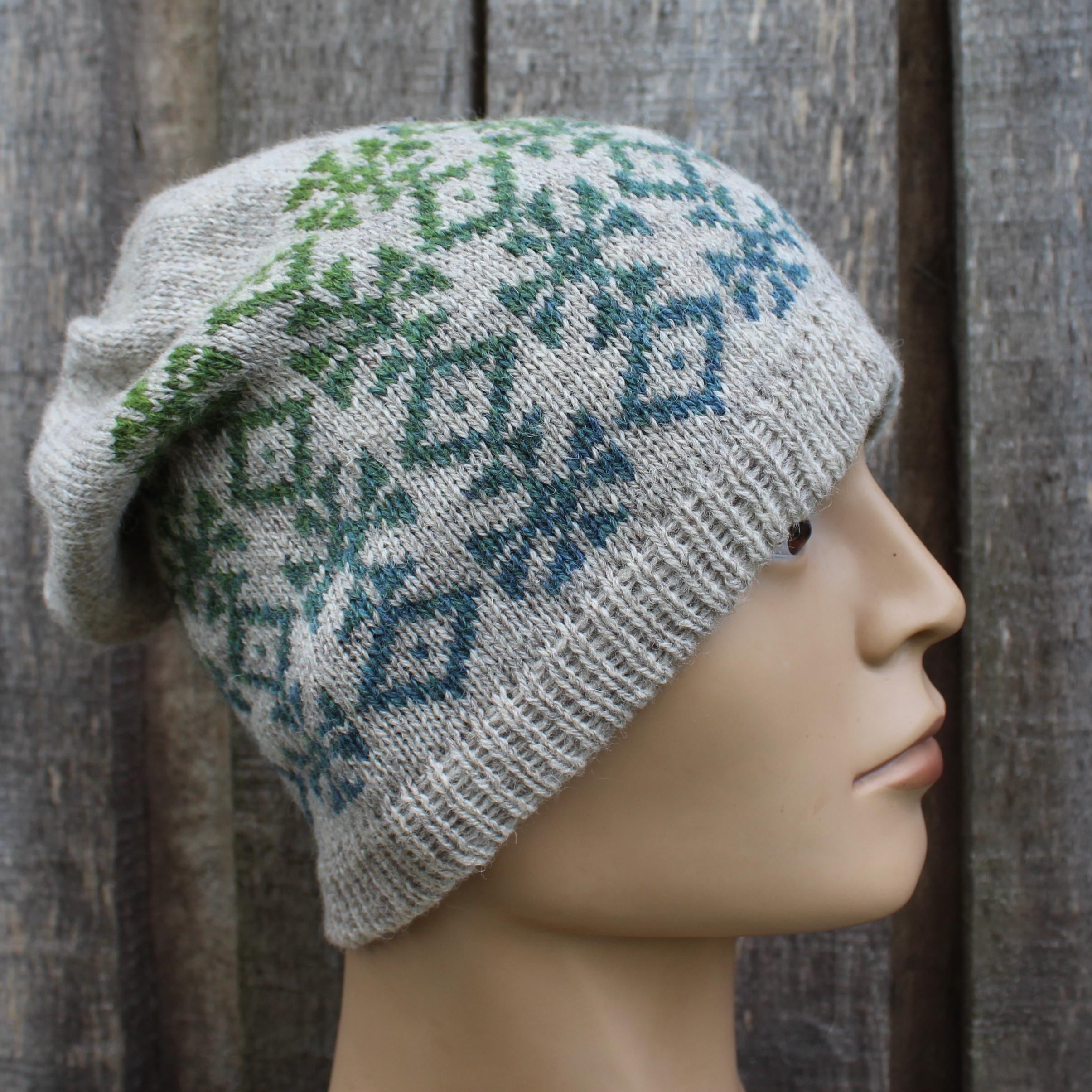 Knitted hat with green and blue pattern on a mannequin head against a wooden background