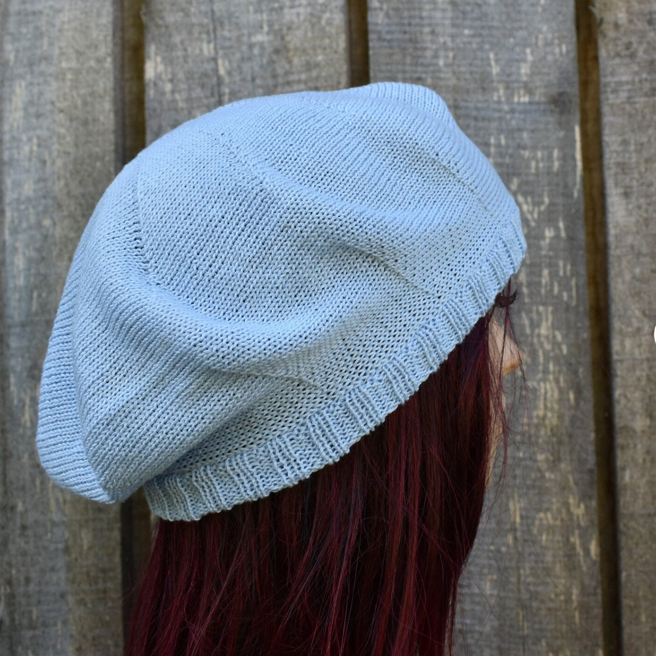 Light blue knit beanie worn by a person with red hair against a wooden background