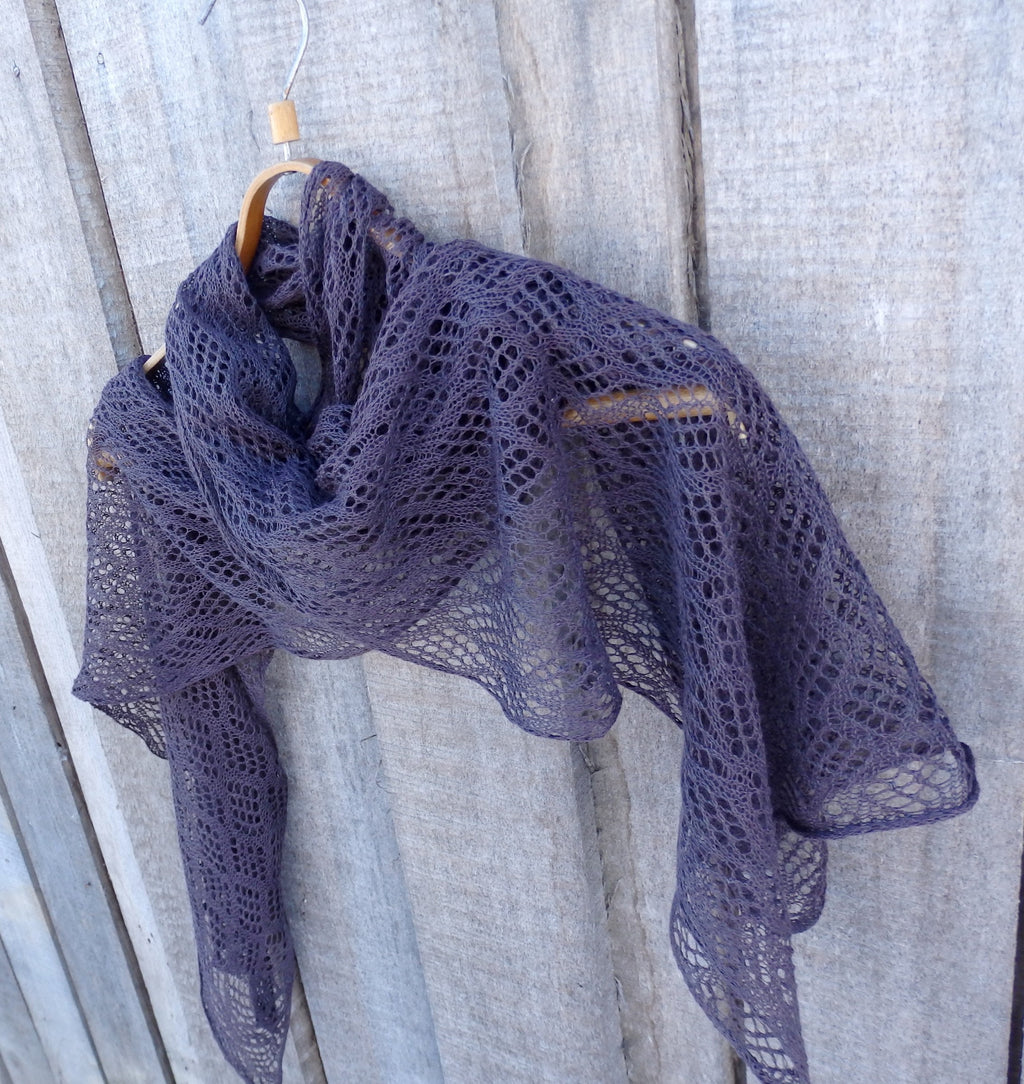 Knitted shawl draped over a wooden hanger against a wooden background