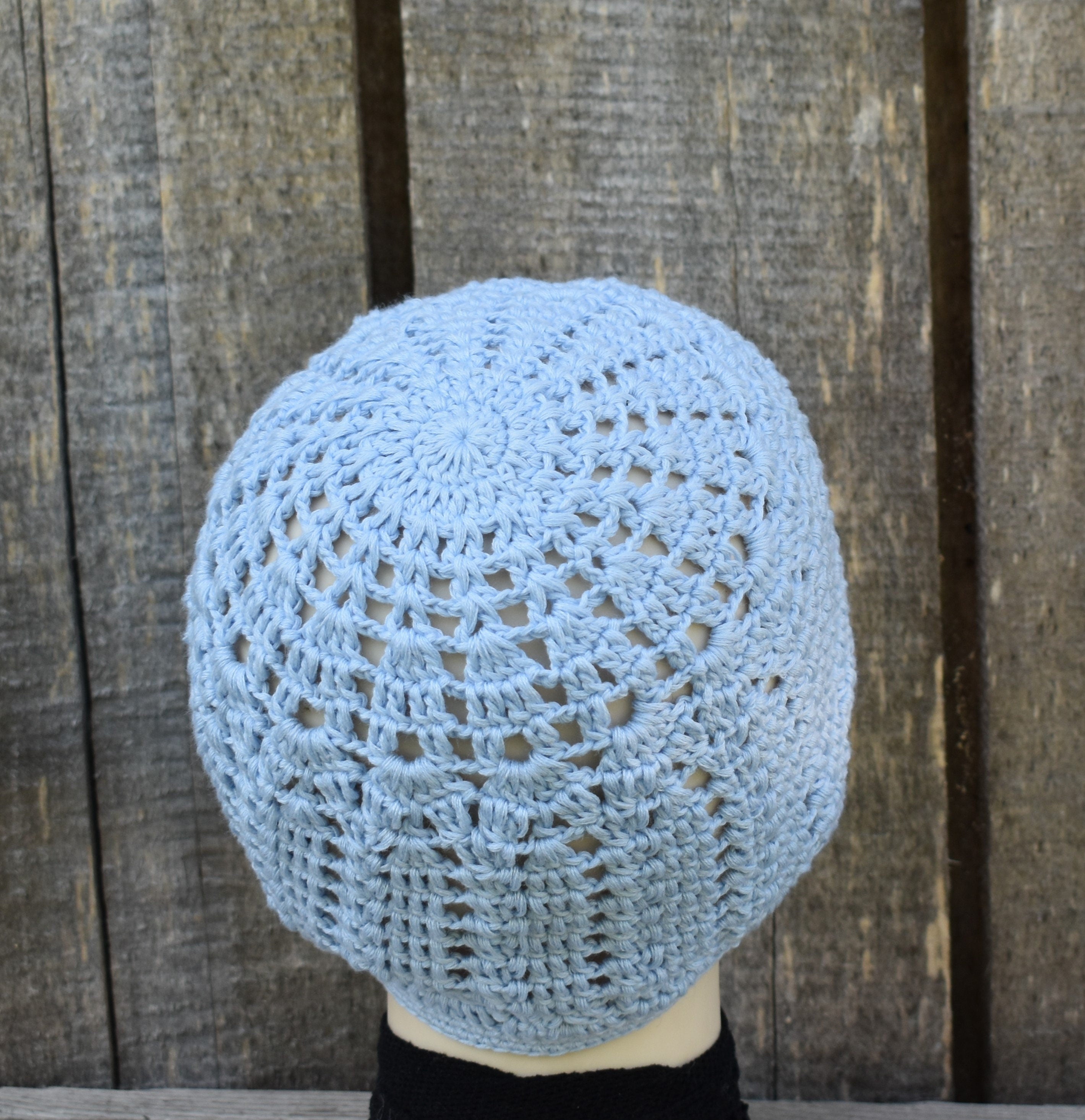 Blue crochet hat on a mannequin head against a wooden background
