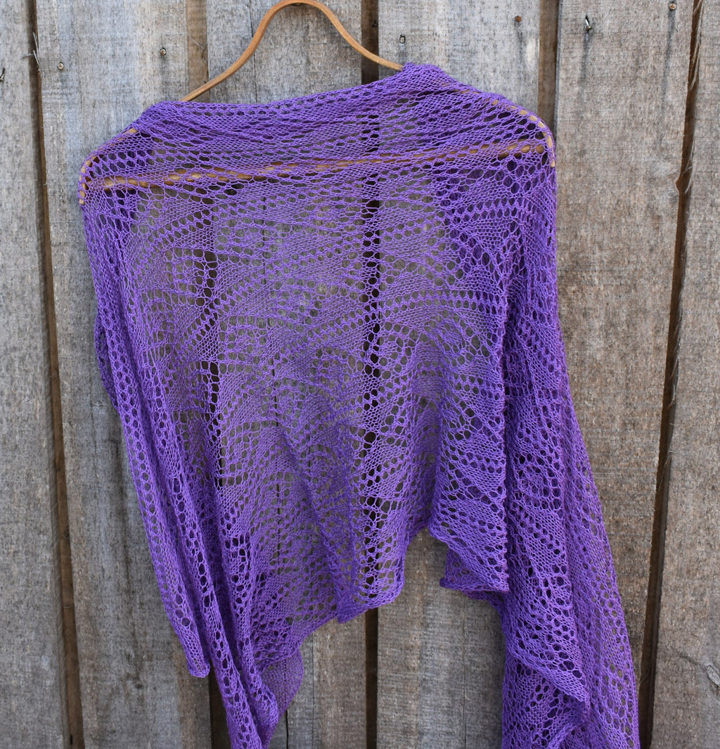 Purple knitted shawl on a wooden hanger against a wooden background