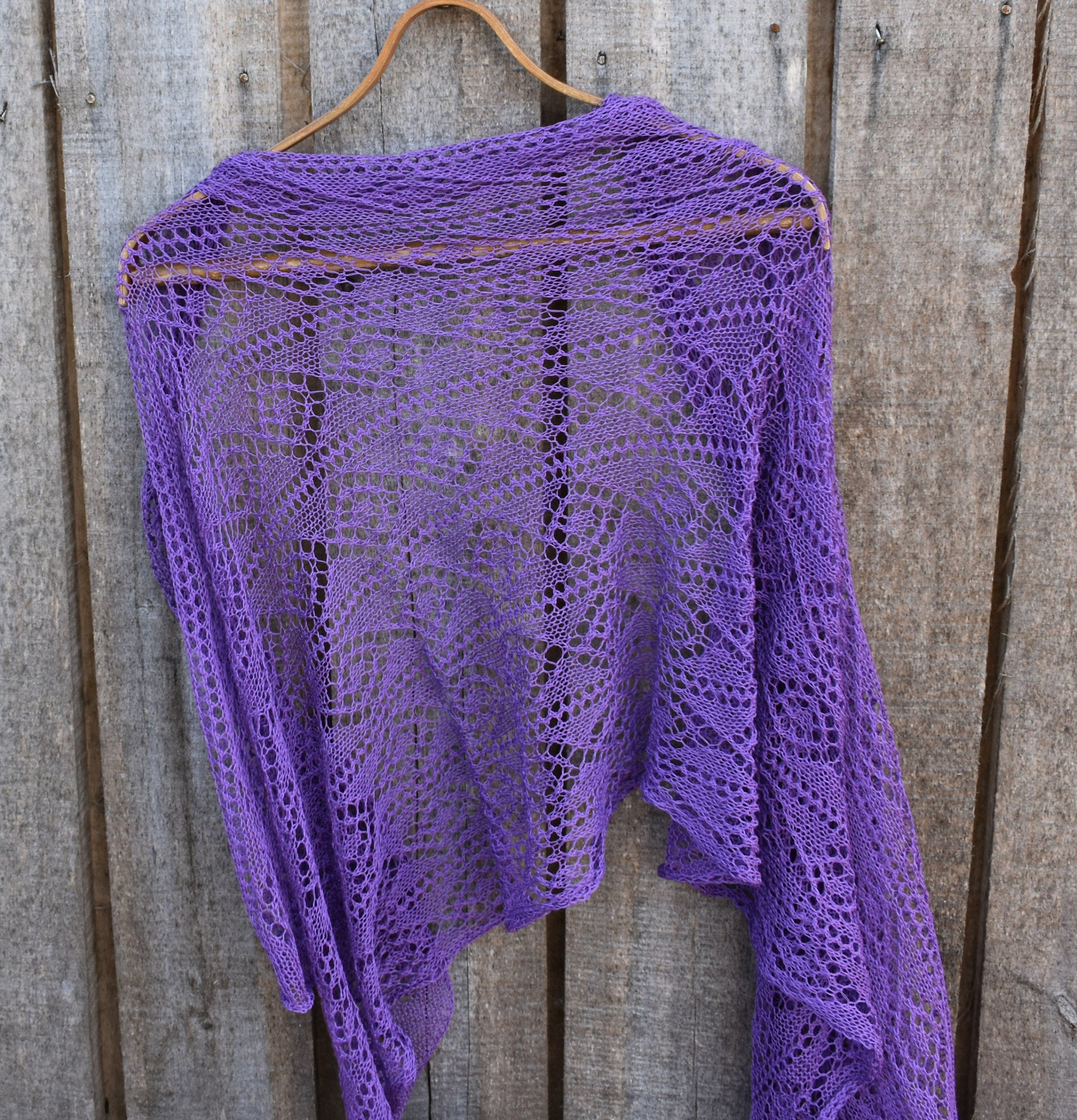 Purple knitted shawl on a wooden hanger against a wooden background