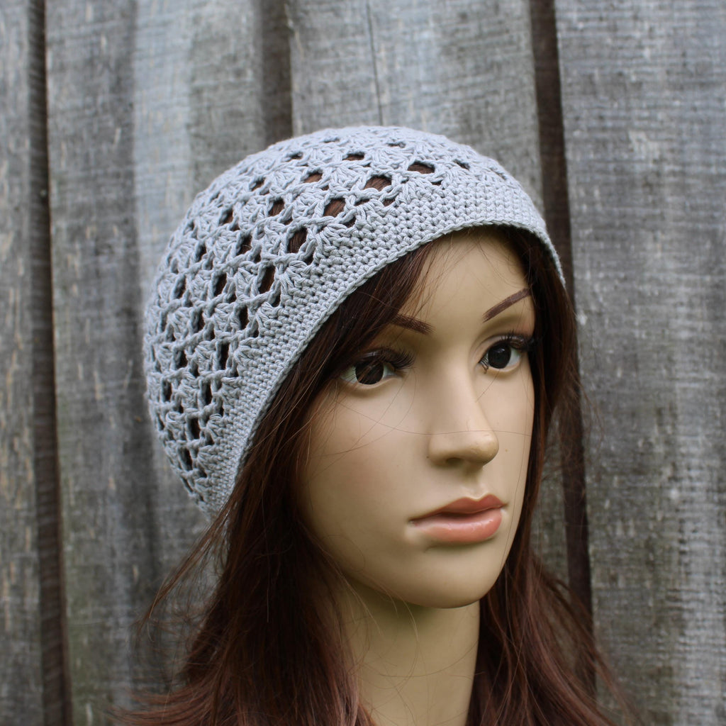 Mannequin head wearing a gray crochet hat against a wooden background