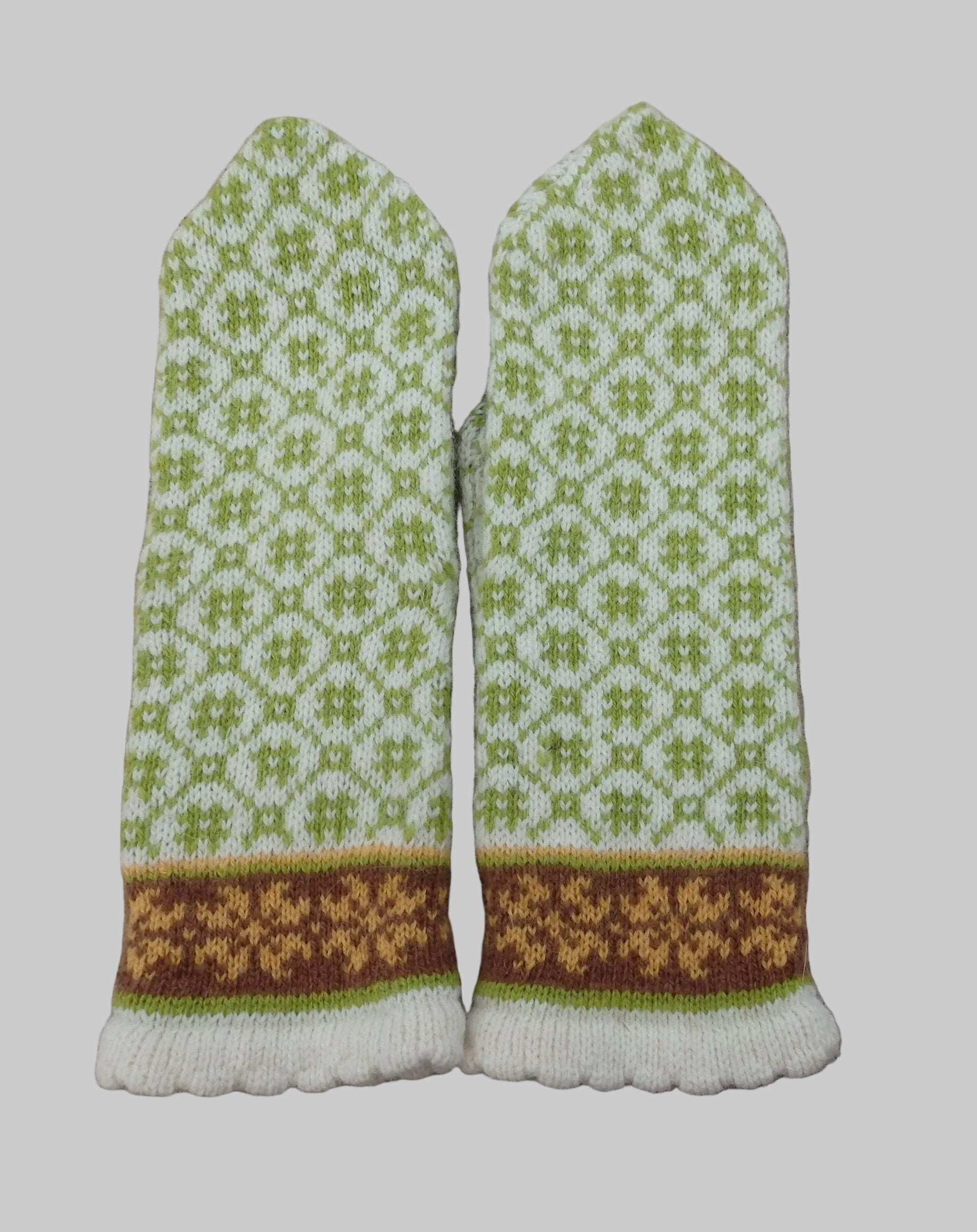 Pair of knitted mittens with green and brown pattern on a textured fabric background