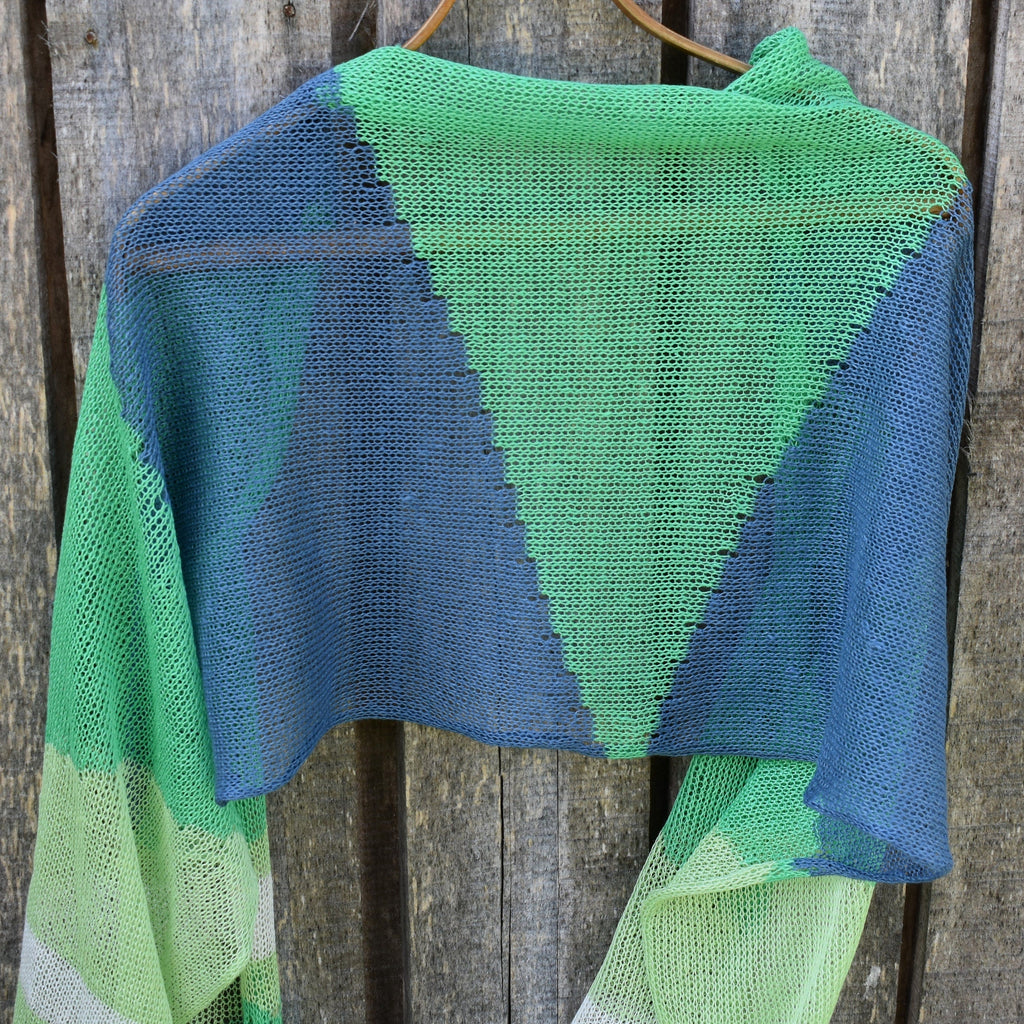 Green and blue knitted shawl hanging on a wooden surface