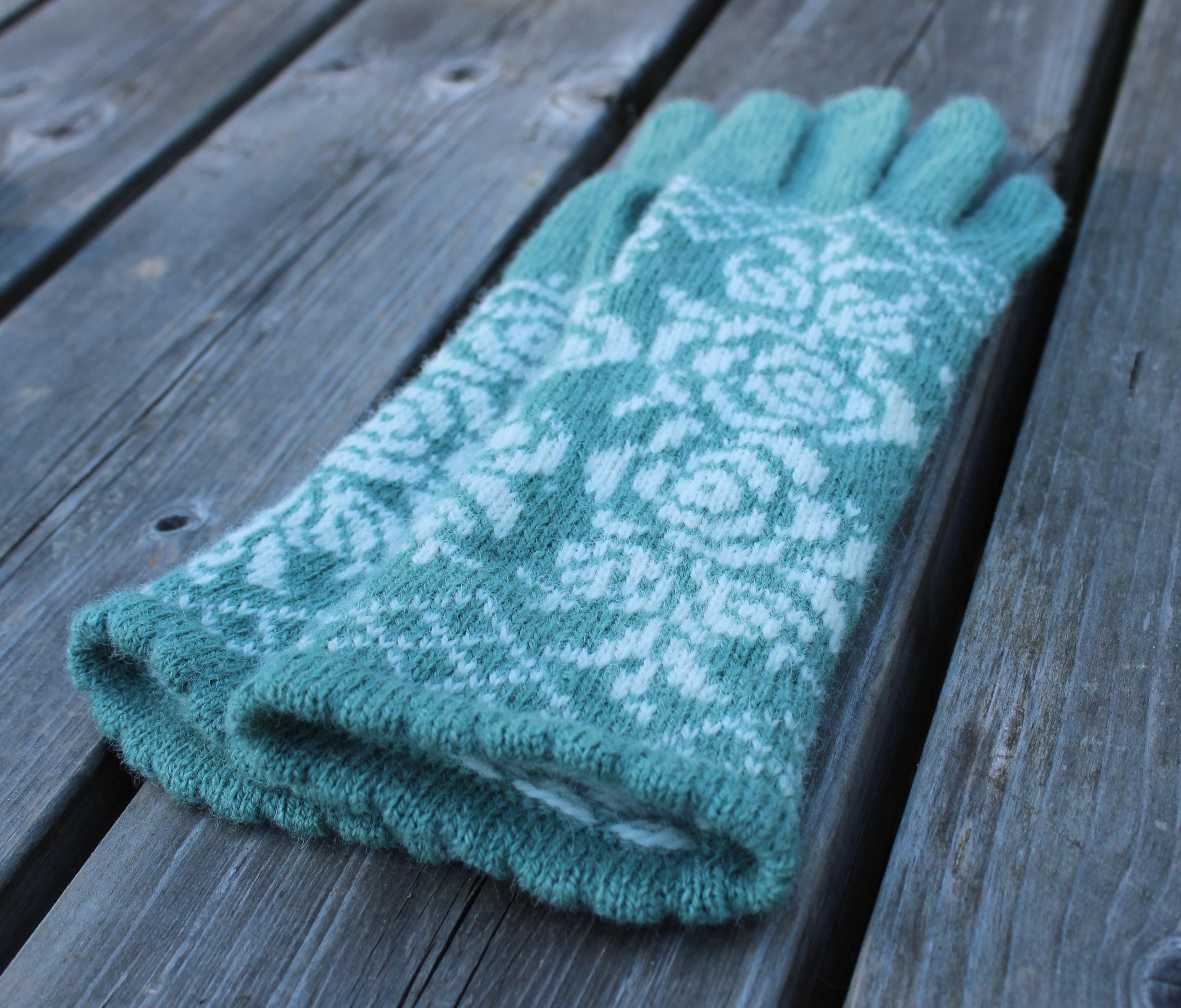 Teal knitted glove with a white pattern on a wooden surface