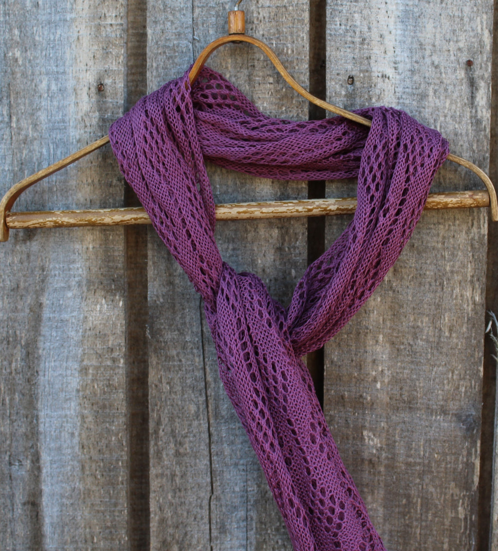 Purple knitted scarf on a wooden hanger against a rustic wooden background