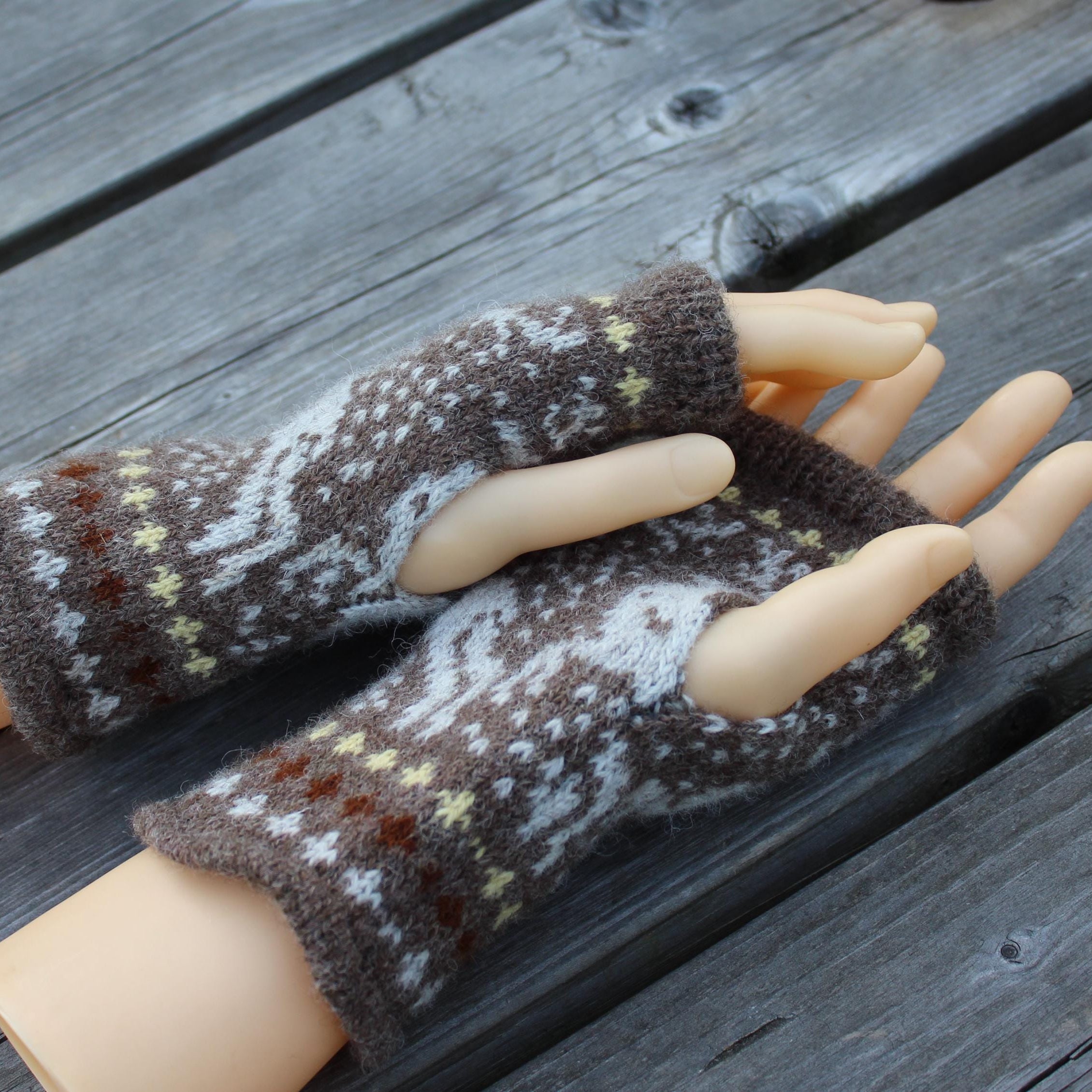 Pair of brown and white patterned fingerless gloves on a mannequin hand against a wooden background