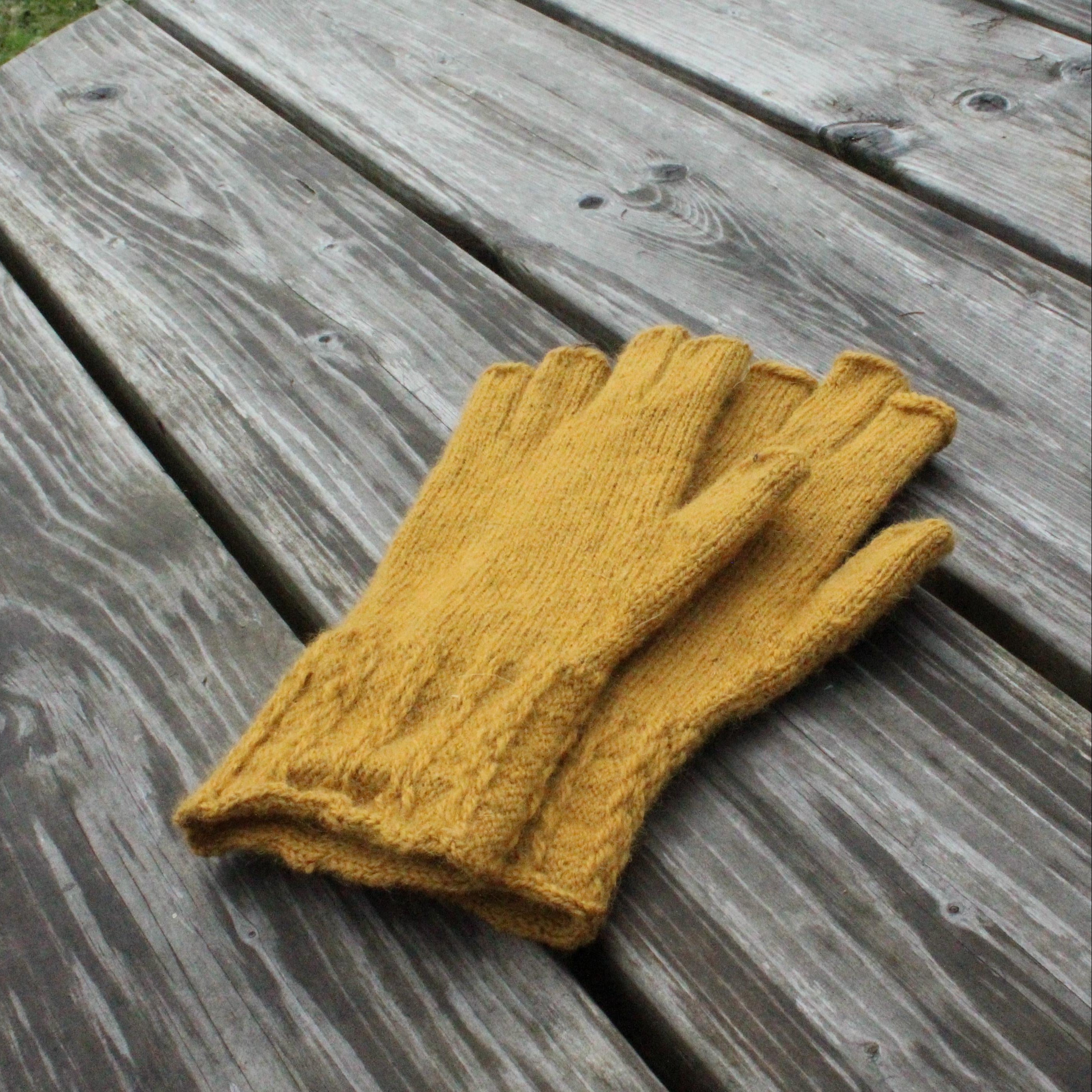 Pair of mustard yellow gloves on a wooden surface