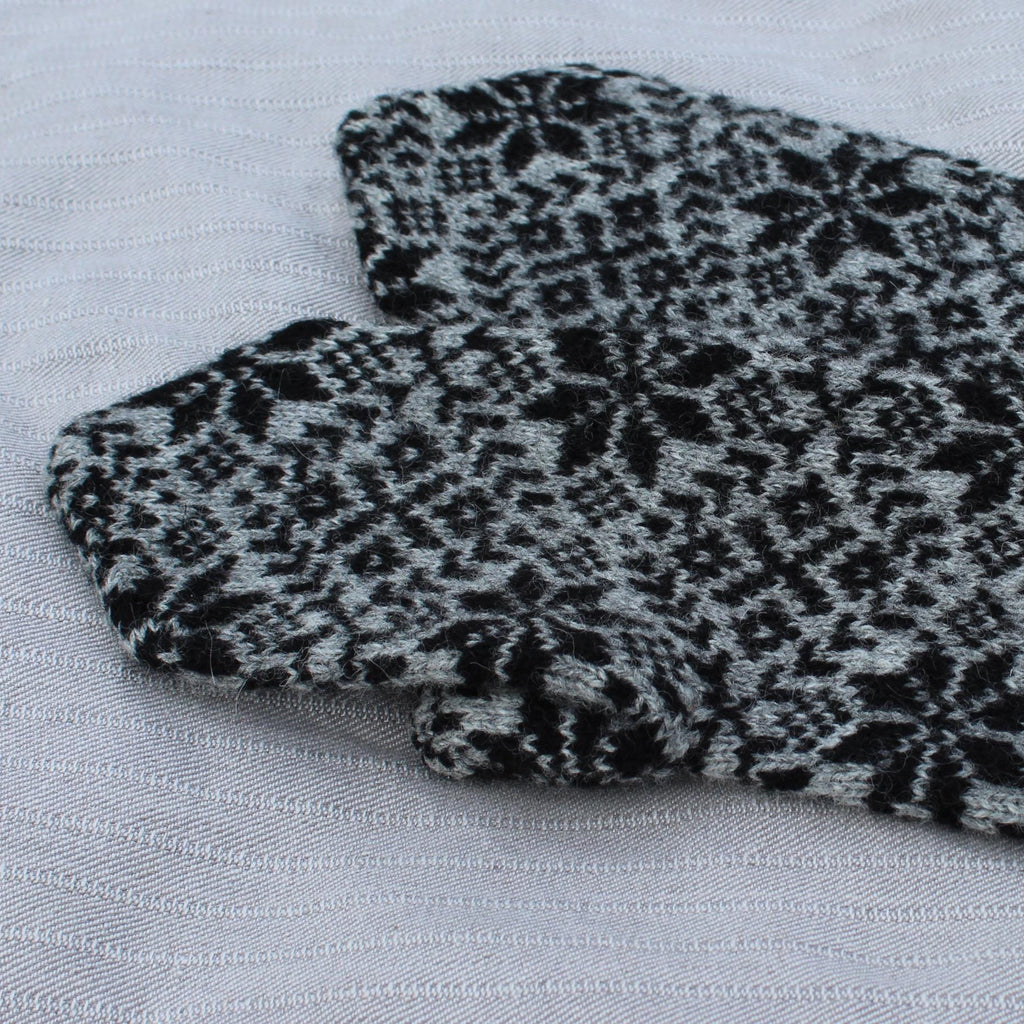 Pair of black and gray patterned mittens with red accents on a light gray background