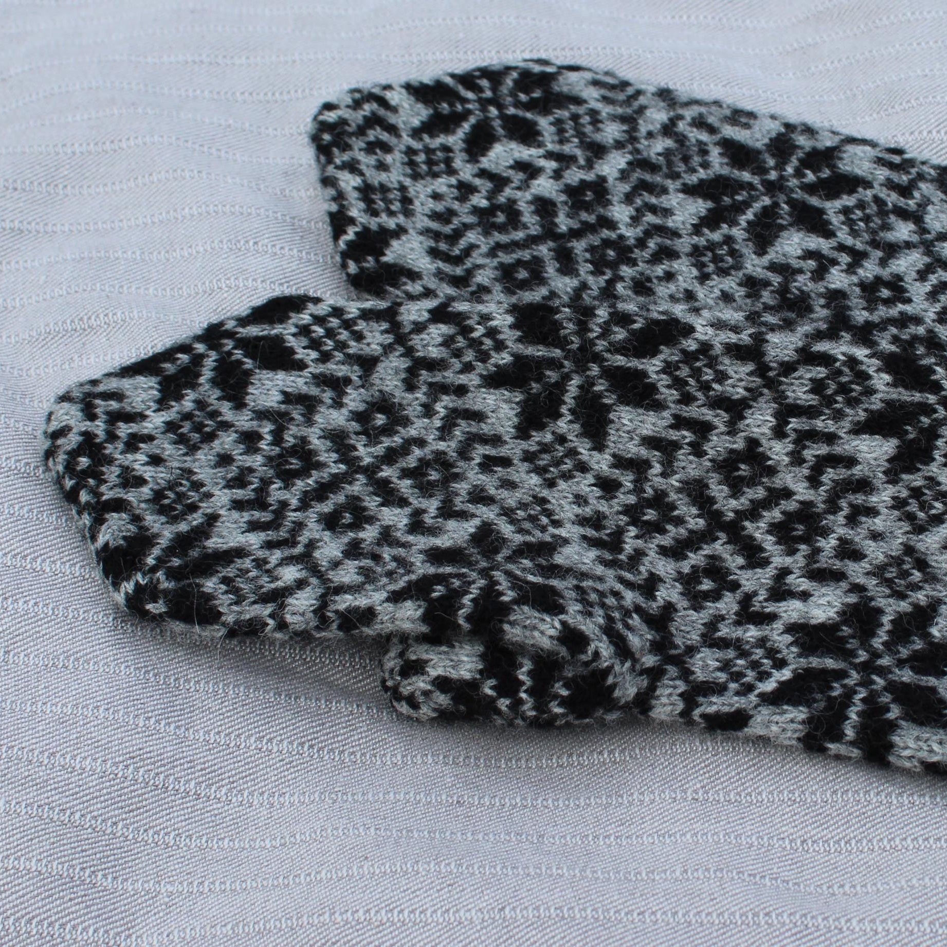 Pair of black and gray patterned mittens with red accents on a light gray background