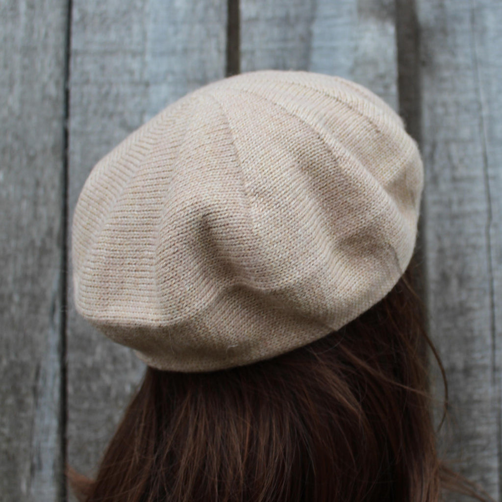 Beige beret worn by a person against a wooden background