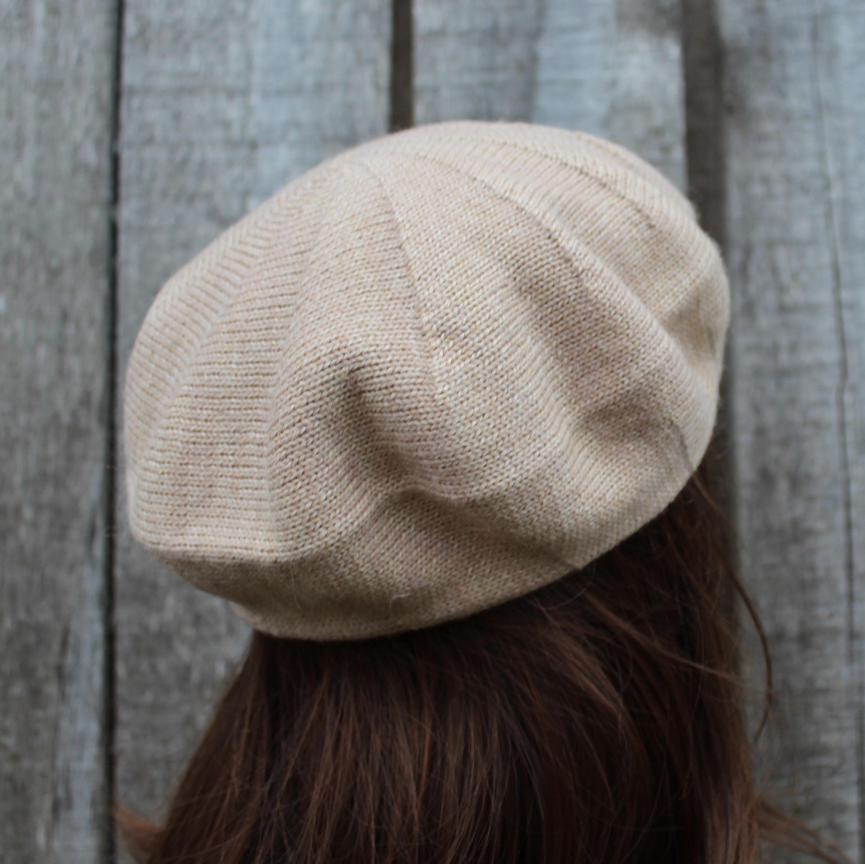 Beige beret worn by a person against a wooden background