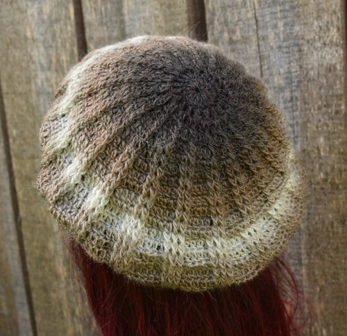 Knitted hat with gradient colors worn by a person against a wooden background