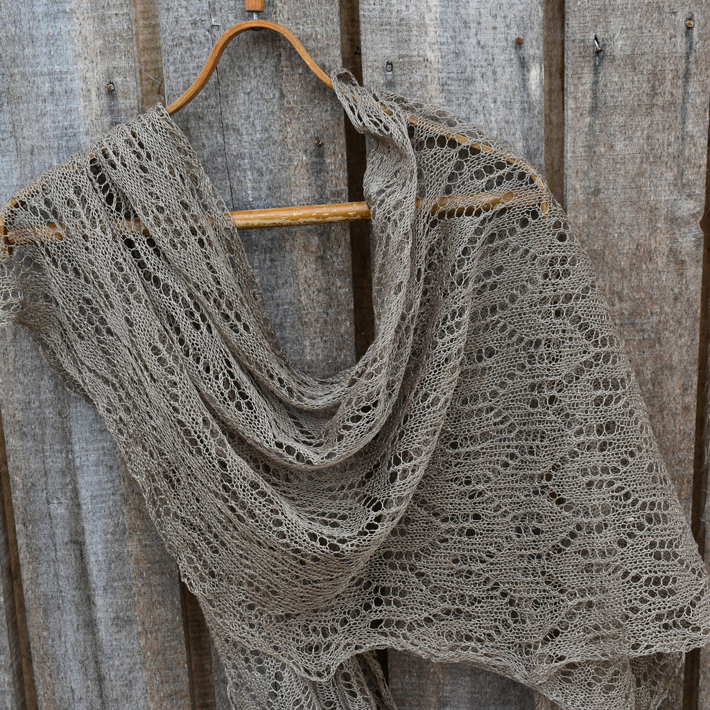 Knitted shawl draped over a wooden hanger against a wooden background