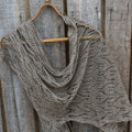 Knitted shawl draped over a wooden hanger against a wooden background