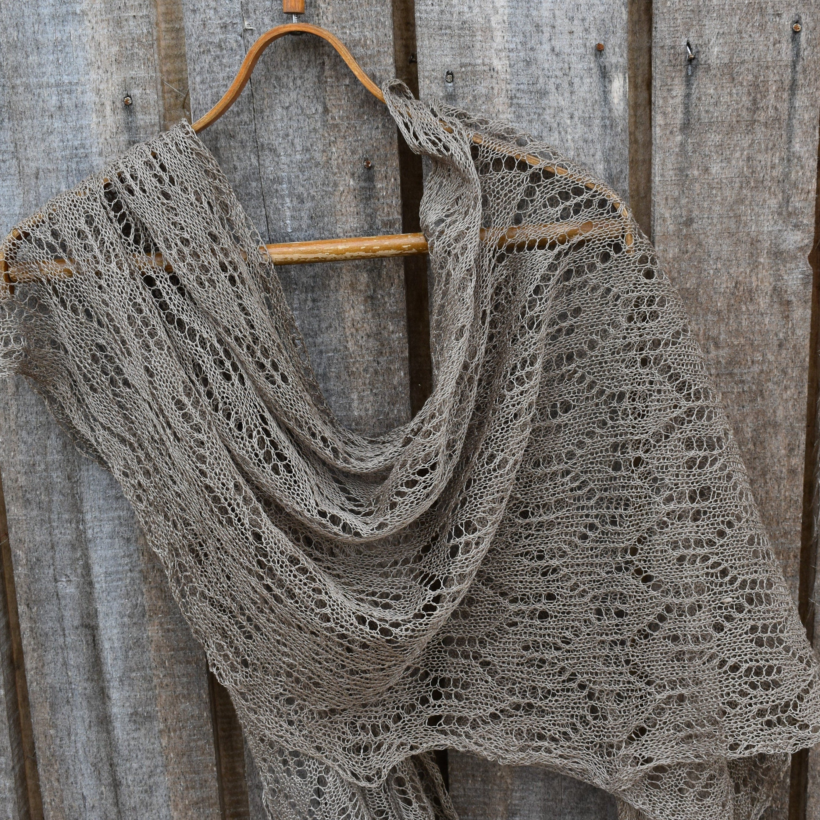 Knitted shawl draped over a wooden hanger against a wooden background