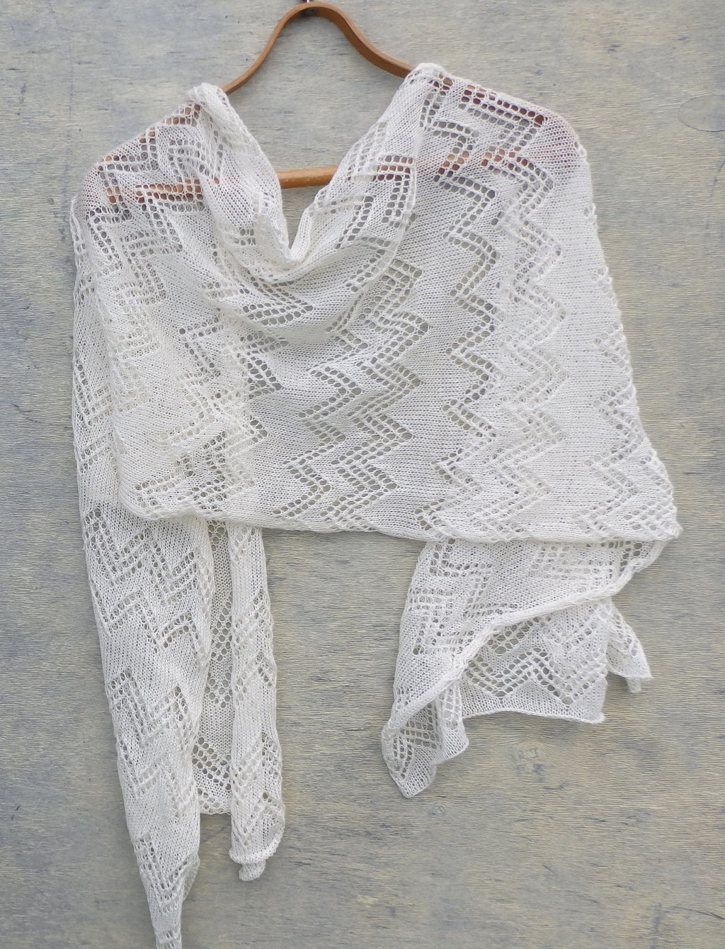 White knitted shawl on a wooden hanger against a gray background