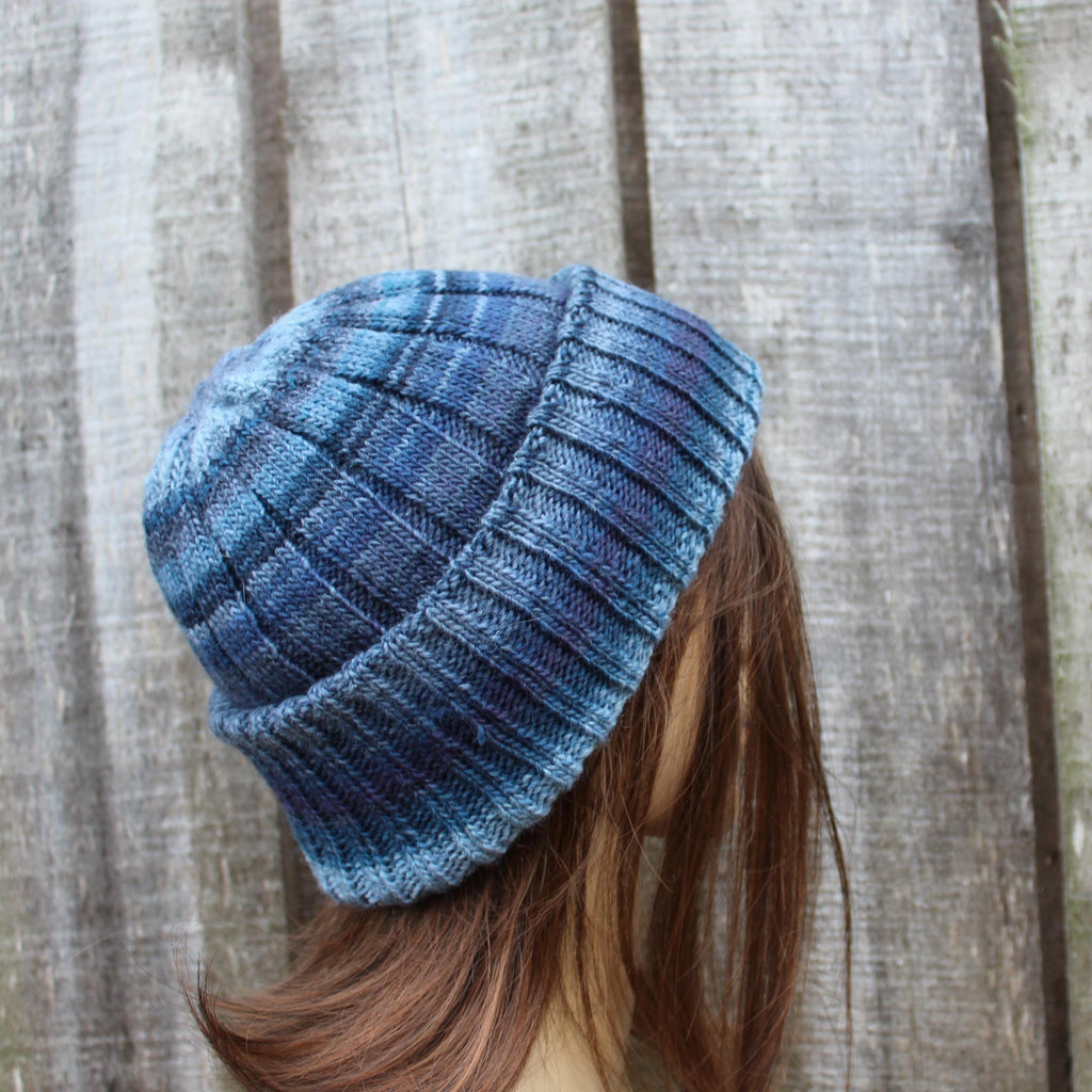 Blue knitted beanie worn by a person with wooden planks in the background