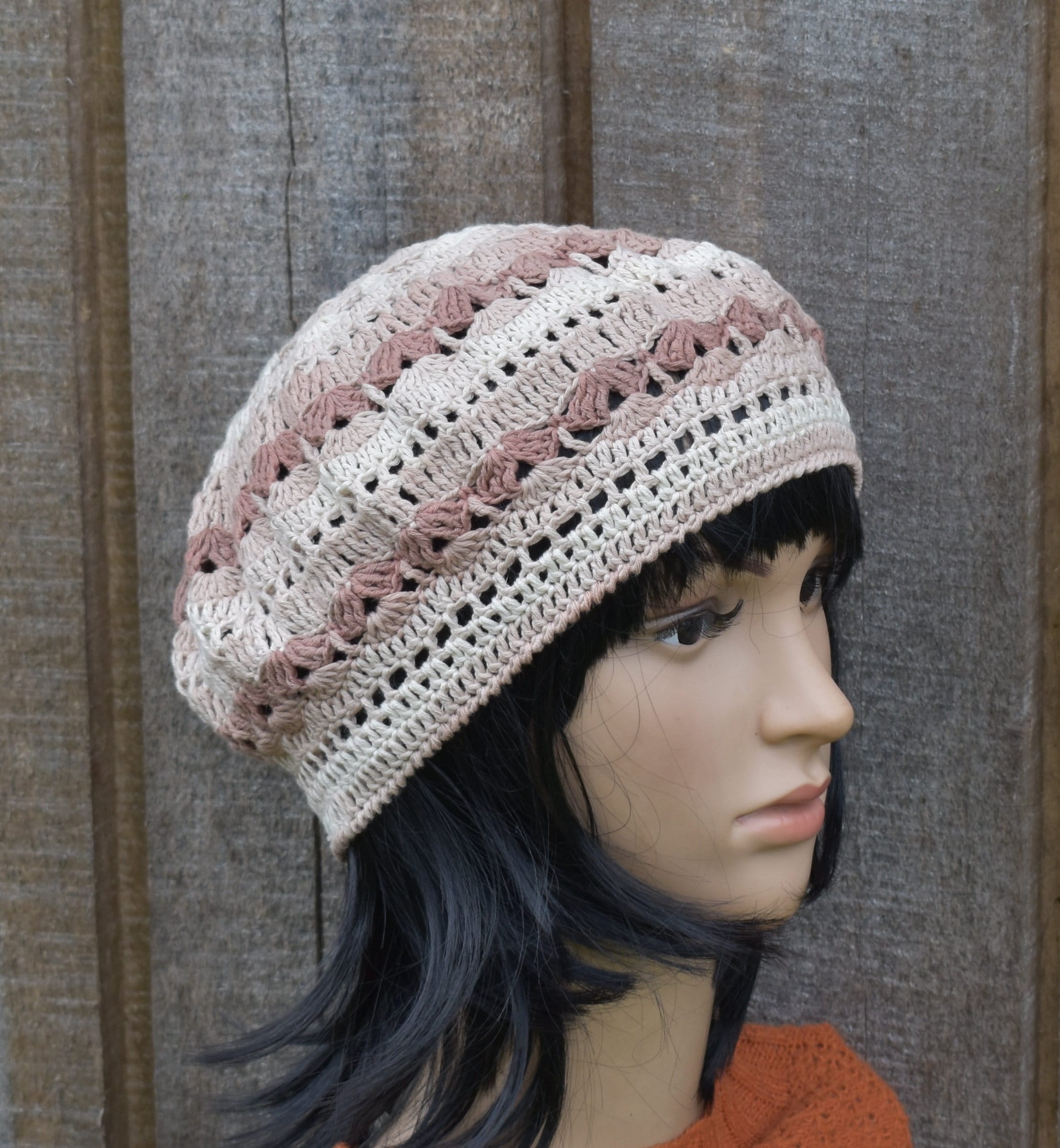Crocheted beanie with pink and white pattern on a mannequin head against a wooden background