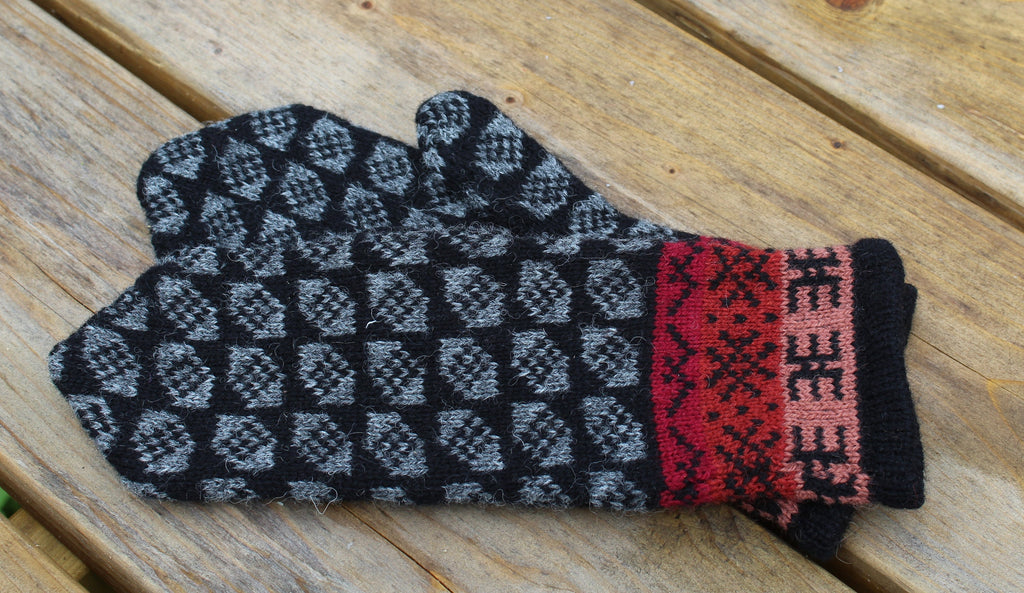 Pair of black and gray patterned mittens with red cuffs on a wooden surface
