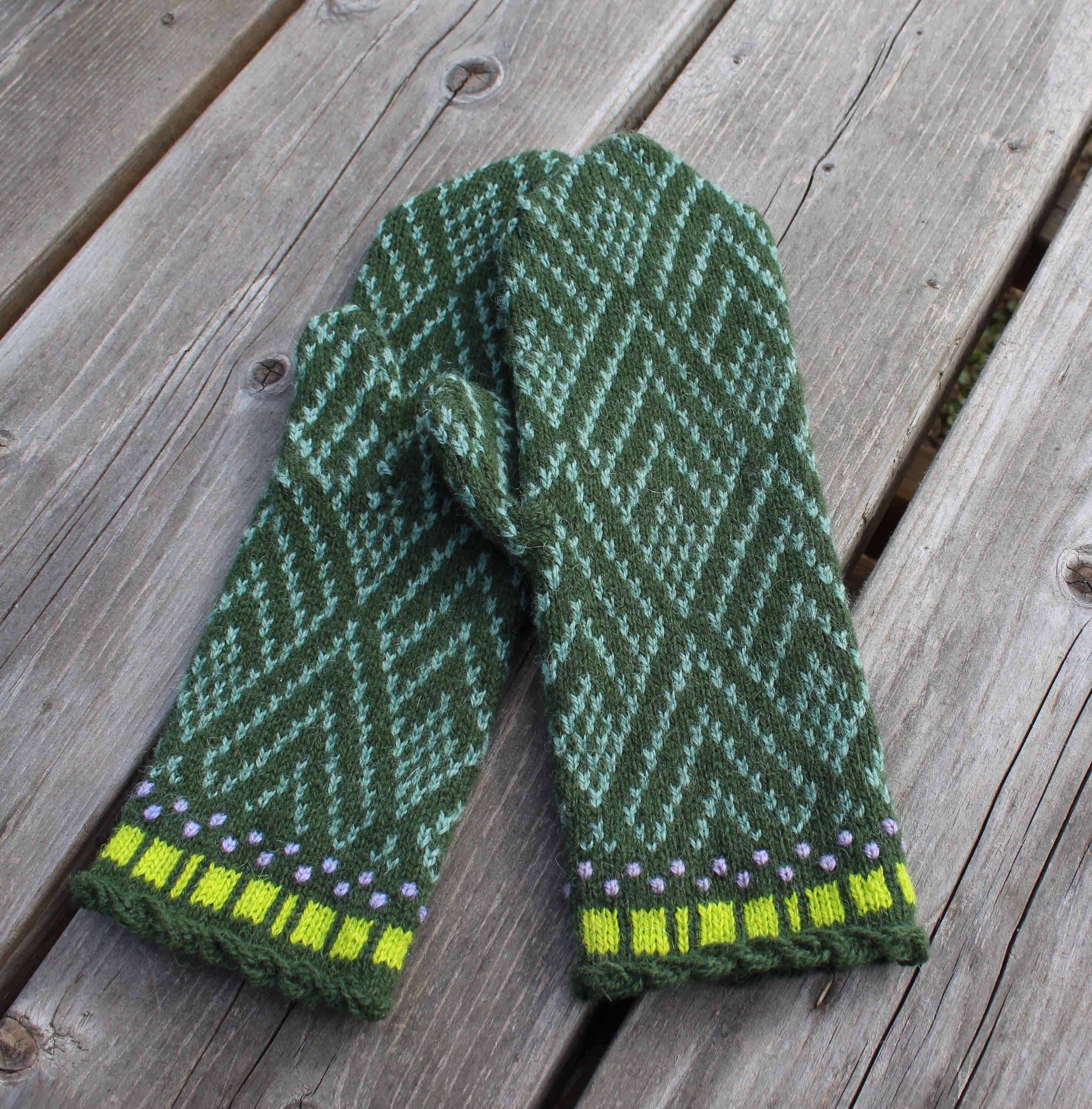 Green knitted mitten with a pattern on a wooden surface