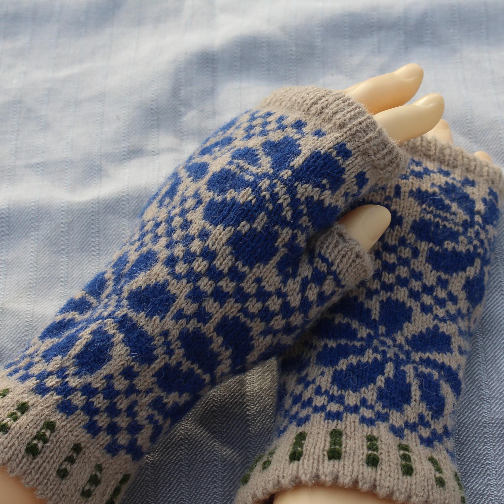 Pair of blue and beige patterned fingerless gloves on a light blue fabric background