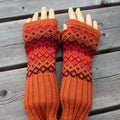 Pair of orange and red knitted fingerless gloves on a wooden surface