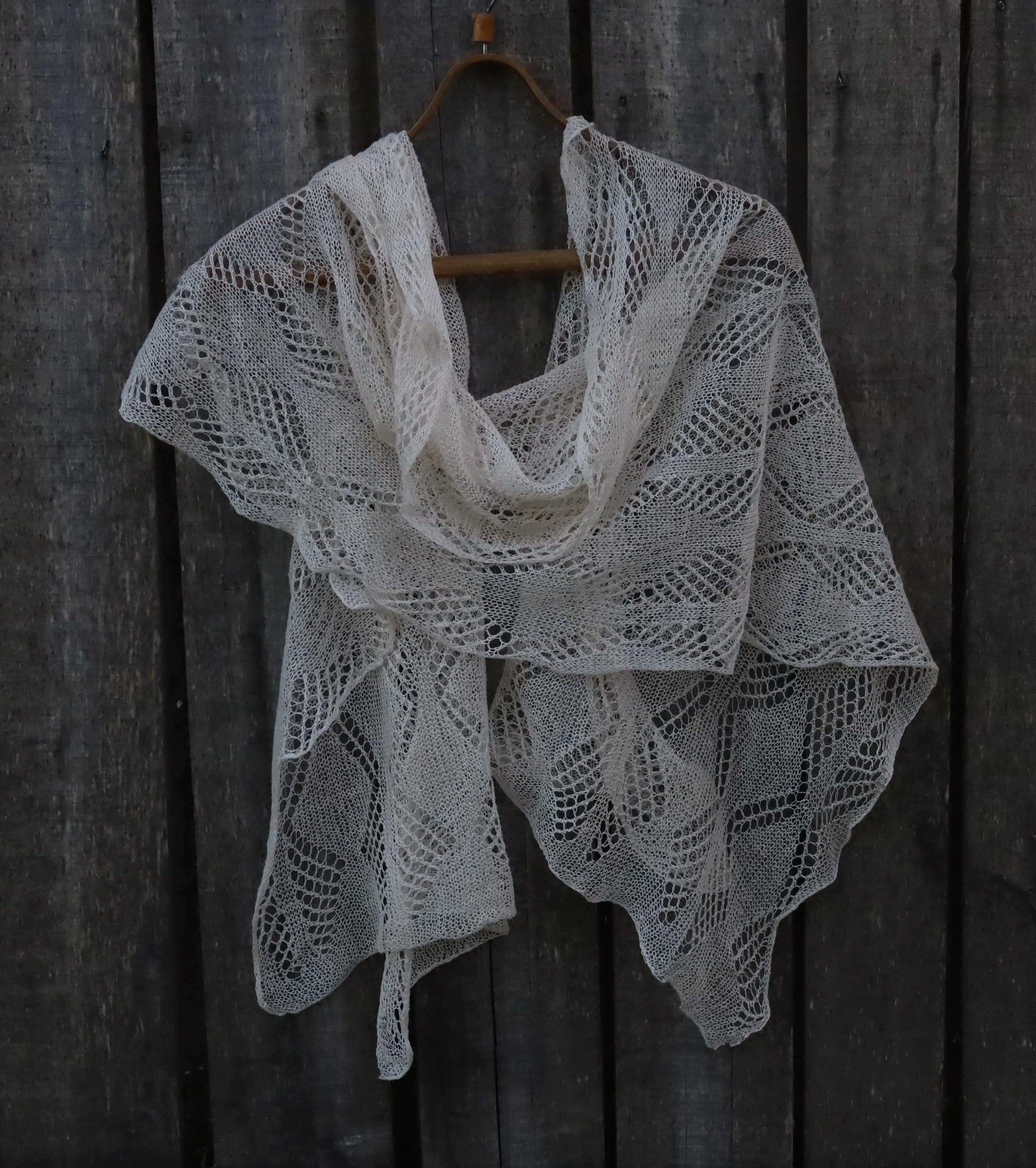 Knitted shawl with a lace pattern hanging on a wooden wall.