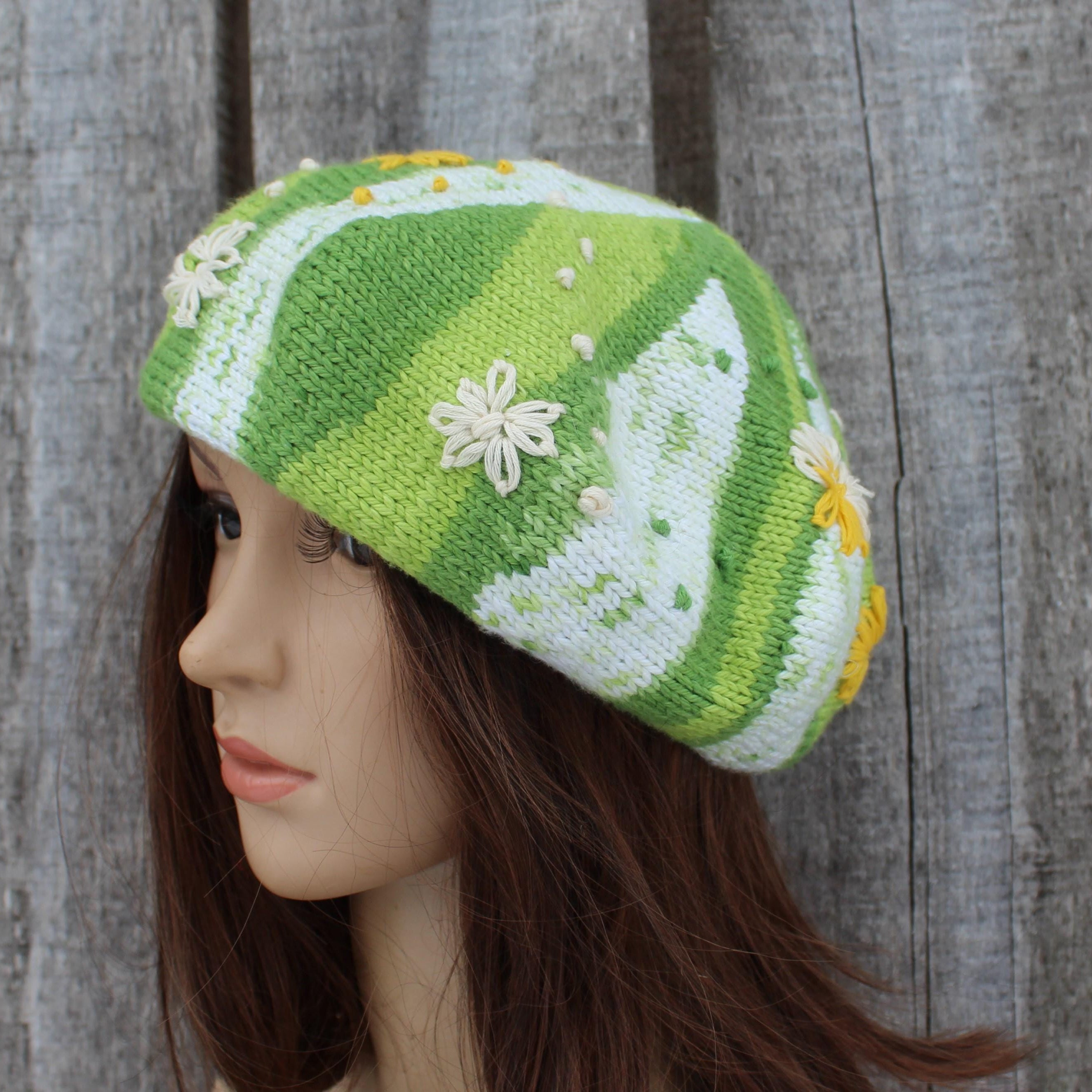 Green and white knitted hat with floral details on a mannequin head against a wooden background