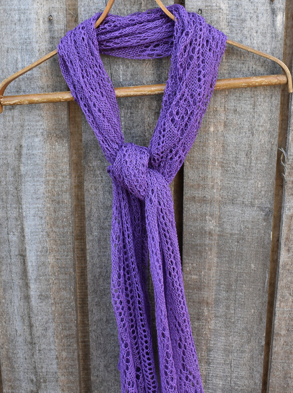 Purple knitted scarf on a wooden hanger against a rustic wooden background