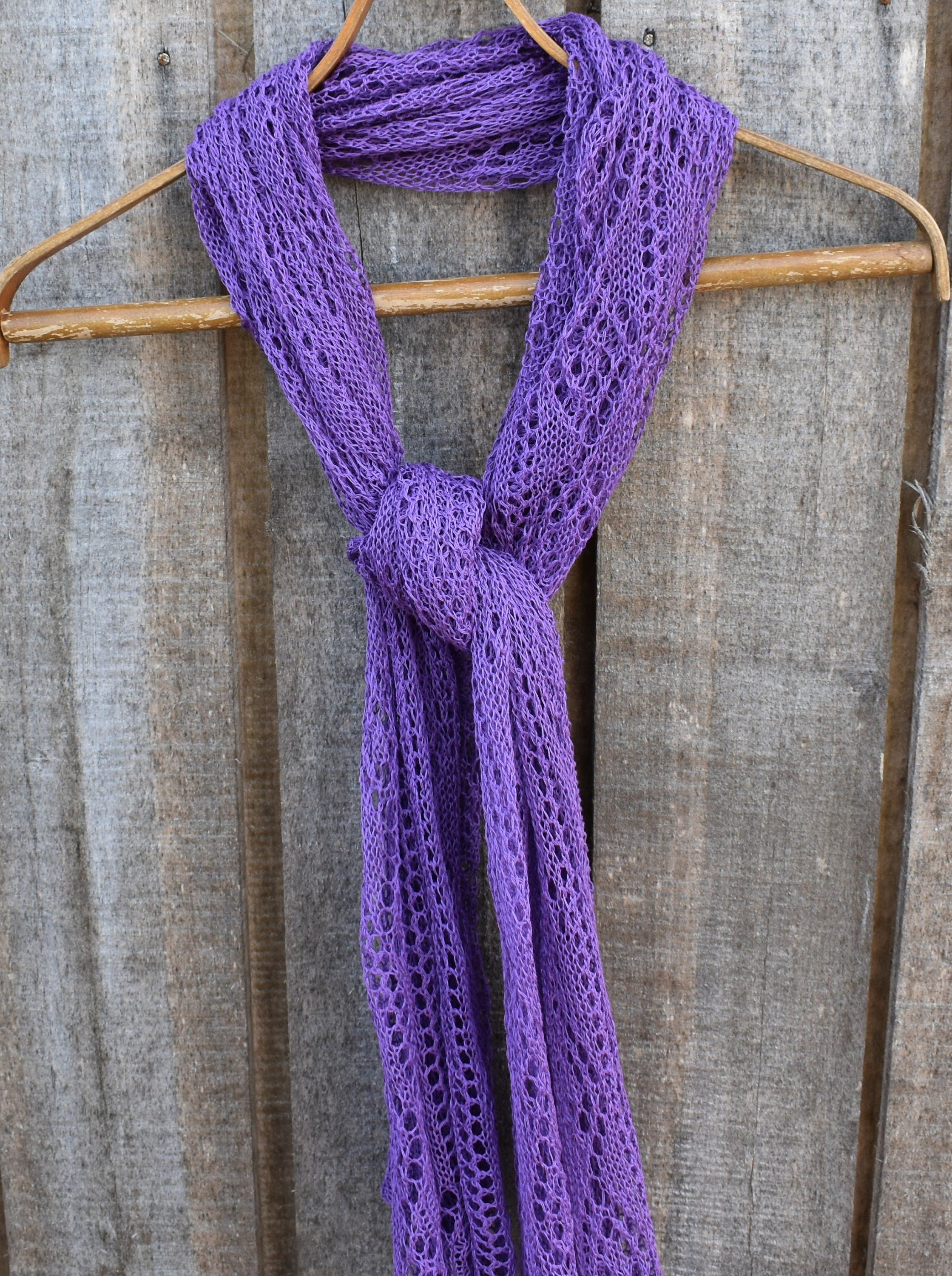 Purple knitted scarf on a wooden hanger against a rustic wooden background